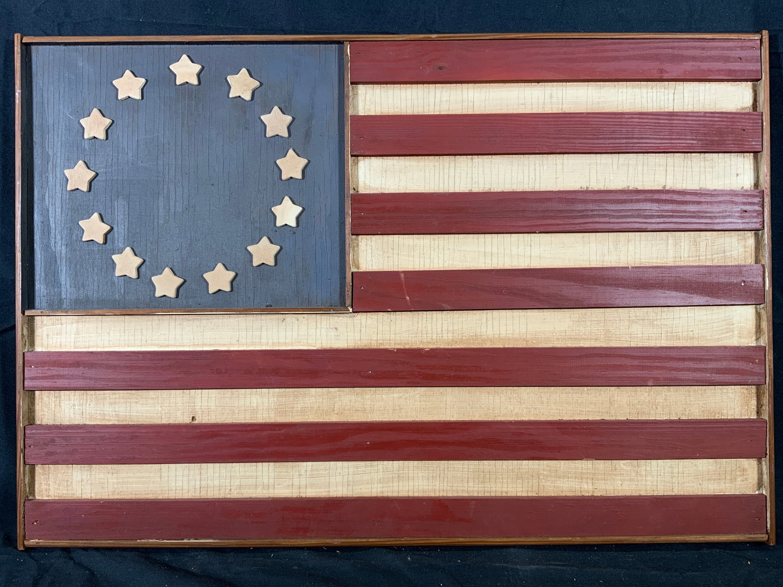 Betsy Ross United States American Flag Wood Plaque: Wooden wall plaque. Subject depicts the United States of Americas original flag design made by Betsy Ross. Plaque measures approx. 24.5 W x 16.5 H in. Debris on wood. Wood is crazing and has some crac