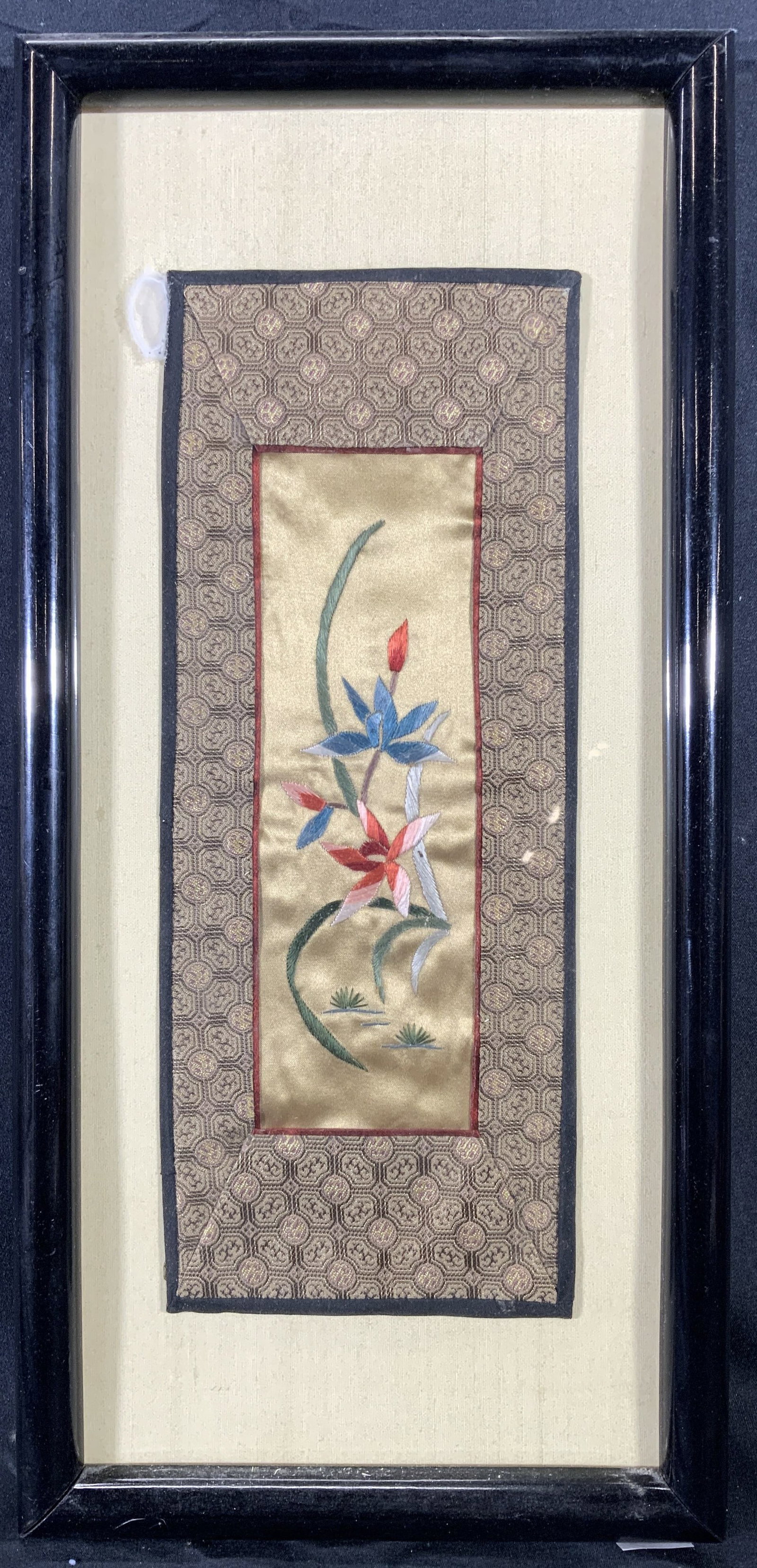 Framed Asian Style Hand Embroidered Silk Lillies: Hand embroidered silk. Subject depicts an Asian style Lillies or lotus flowers and foliage. Bordered with an Asian style pattern. Framed in a black wooden frame. Frame measures approx. 7.5 W x 15.5 H 