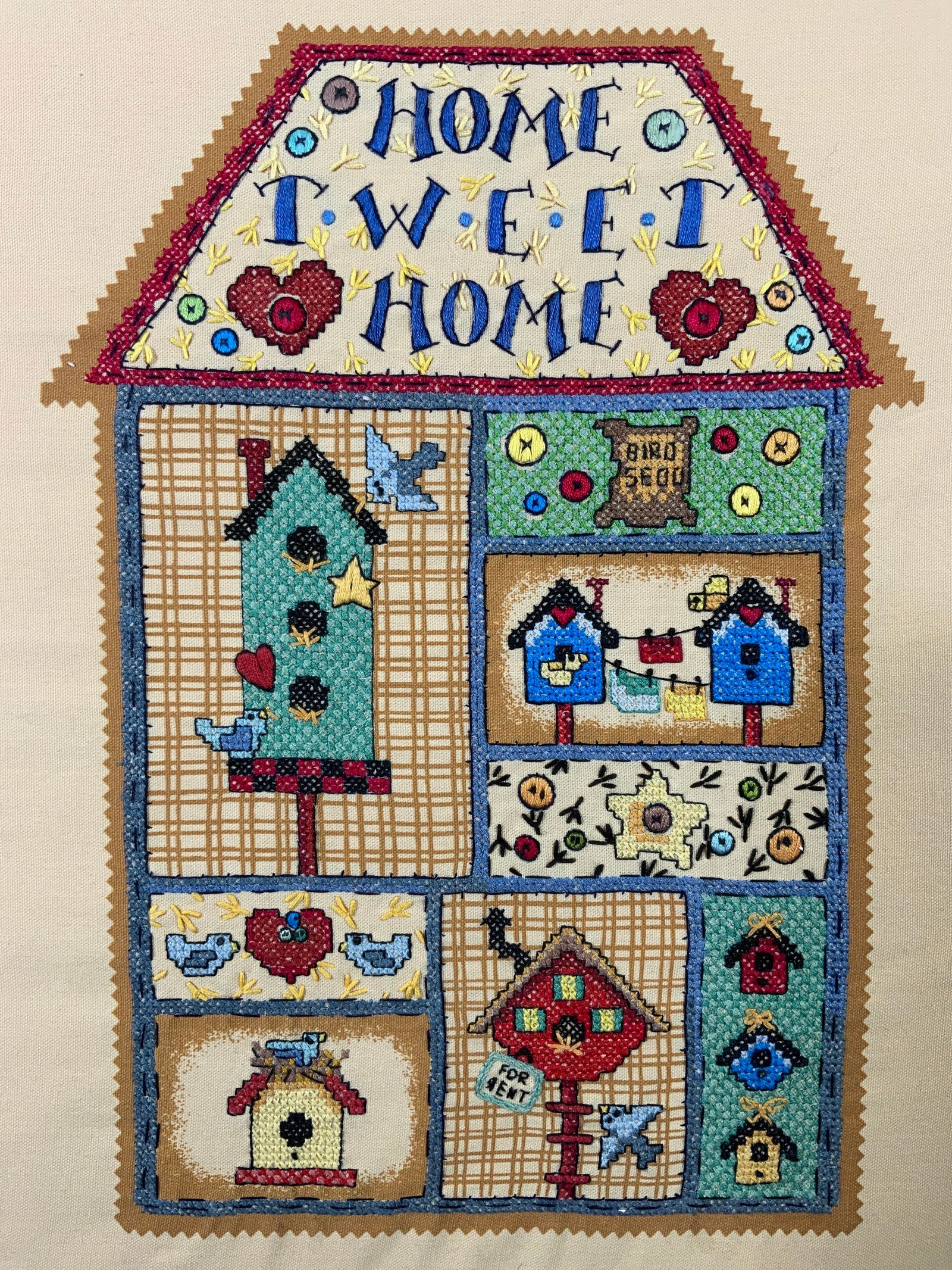 Stamped Cross Stitch Home Tweet Home Sampler: Cross stitch fabric sampler on board. Subject depicts a home with a different motif in each room. Top of house reads Home Tweet Home. Other motifs include, bird houses, bird seed, birds foot steps, an