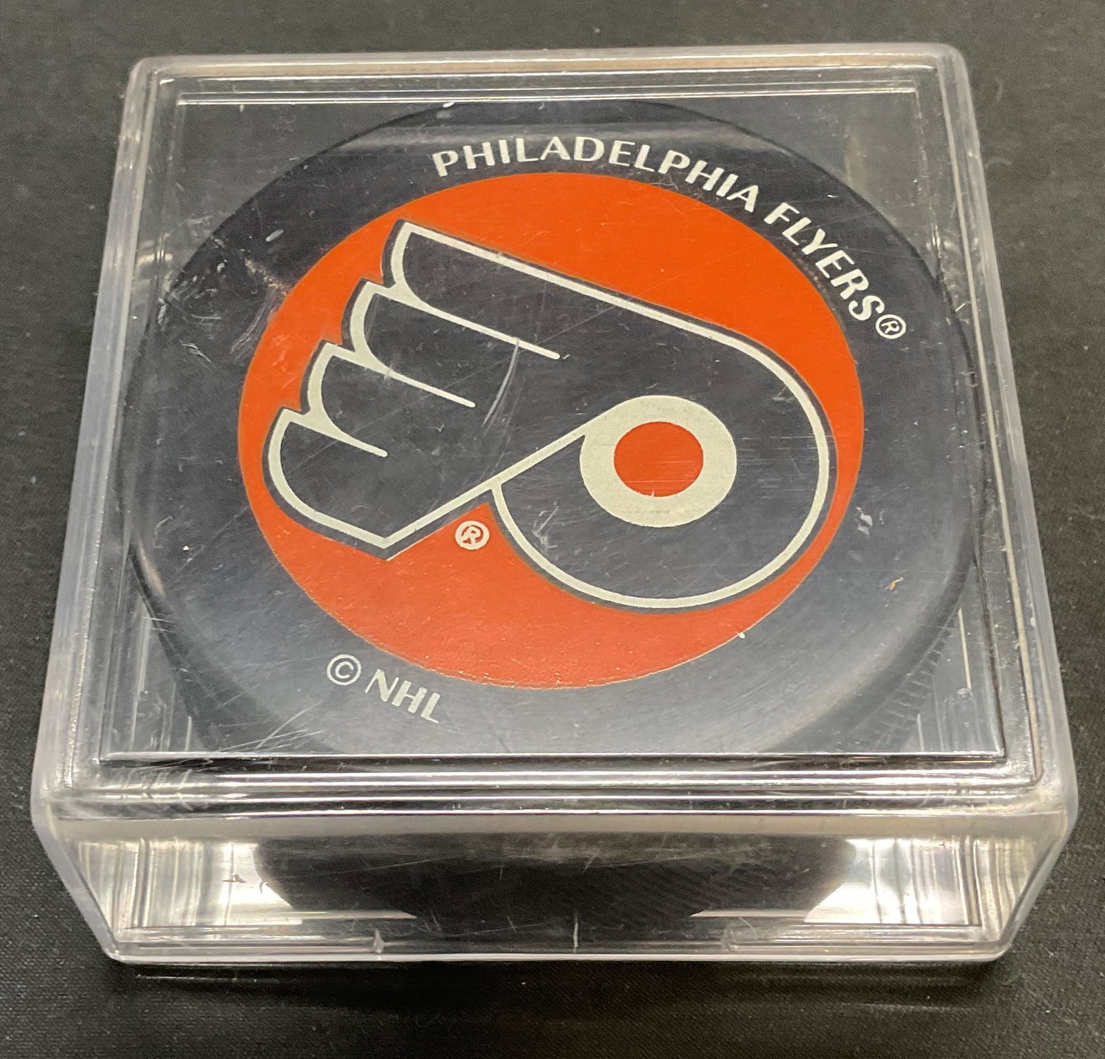 Official NHL Philadelphia Flyers Hockey Puck: Officially licensed NHL Philadelphia Flyers hockey puck by Puck World. Includes acrylic case. Puck measures approx. 3 x 1 inches. Some wear to case consistent with exposure. Property of Fifth Avenue, 