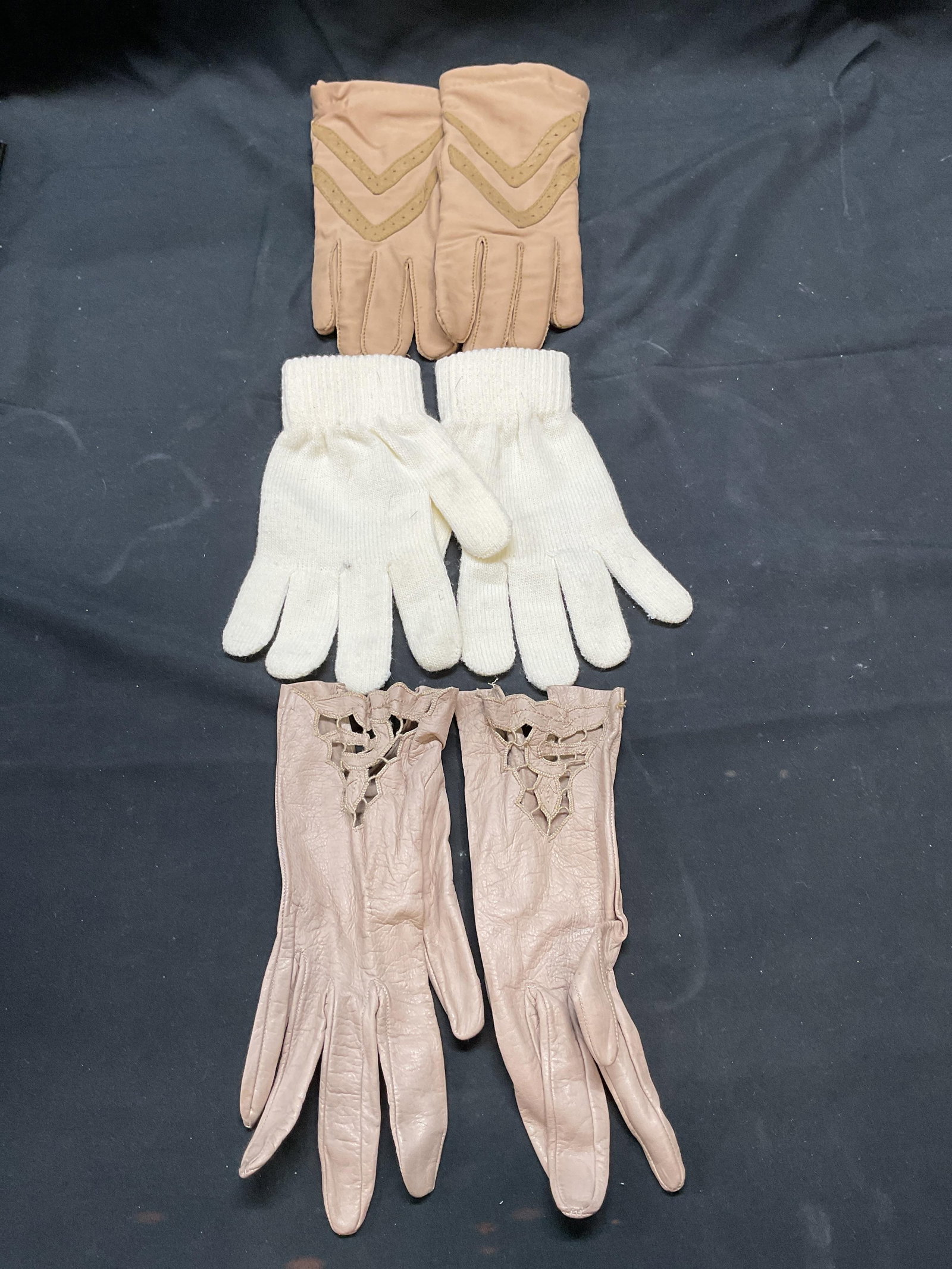Lot 3 Isotoner Tan Gloves, More: Isotoner tan gloves, nylon blend. ABG white gloves. Acrylic blend. Beige leather gloves with cutout detail. Largest pair measure approx, 9 inches long. All pieces have some wear to material consistent