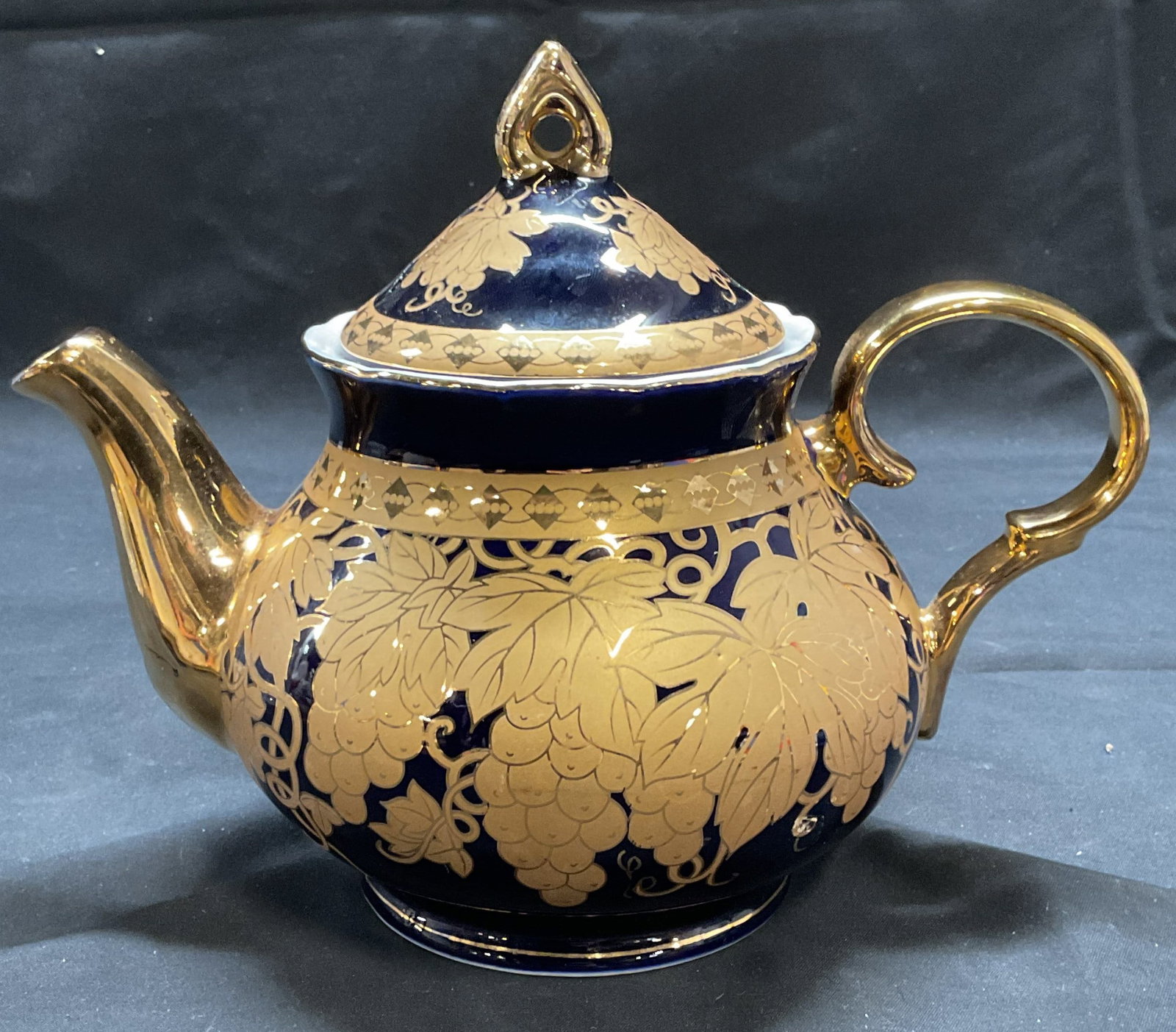 Czech Republik Kobalt Gilt Porcelain Teapot: Gilt porcelain teapot in cobalt blue with grape design. Marked Czech Republik Original Kobalt on underside. Measures approx. 9.5 x 5.5 x 7 inches. Some surface wear including scratching observed. Porc