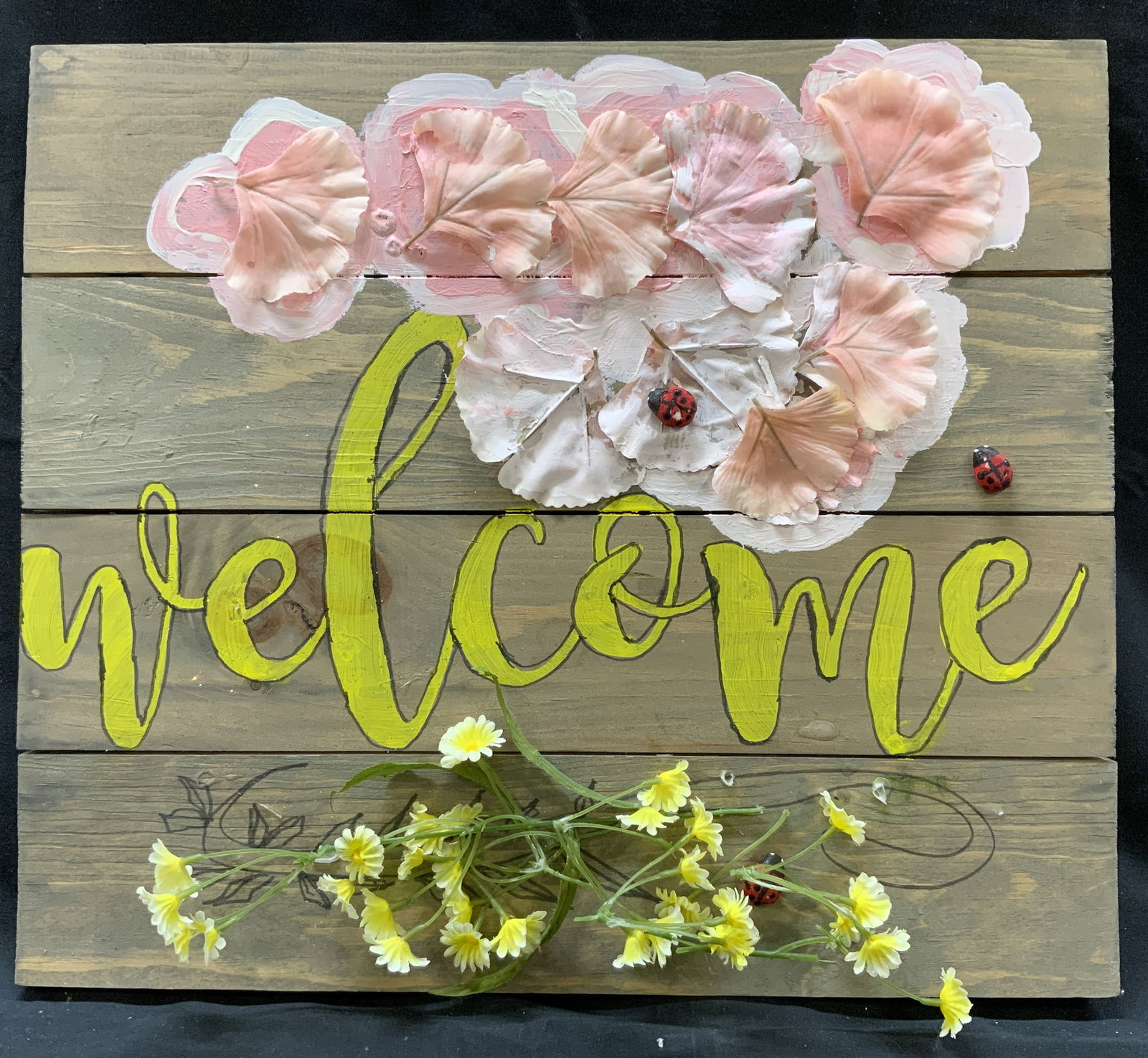 Hand Painted Wooden Floral Welcome Sign: Hand painted wooden sign. Sign reads Welcome in yellow script. Sign has composite and fabric flowers affixed to board with background behind the painted the same color. Sign measures approx. 16 W x 14