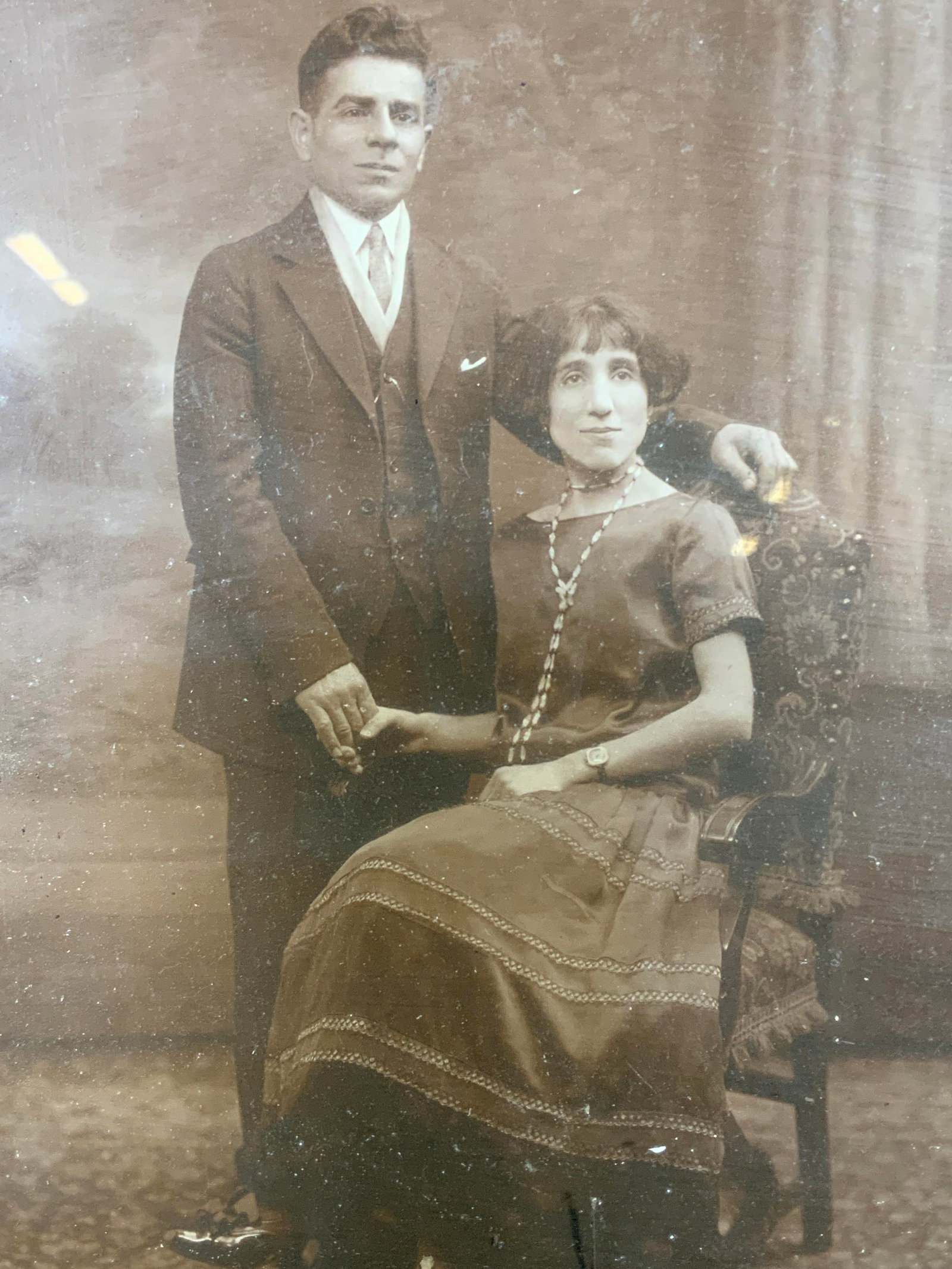 Framed Vintage Married Couple Photograph: Photograph on paper. Subject depicts an Antique photograph of a couple, with the woman sitting in a chair and a man standing next to her holding her hand. Framed in a black wooden frame. Frame measure