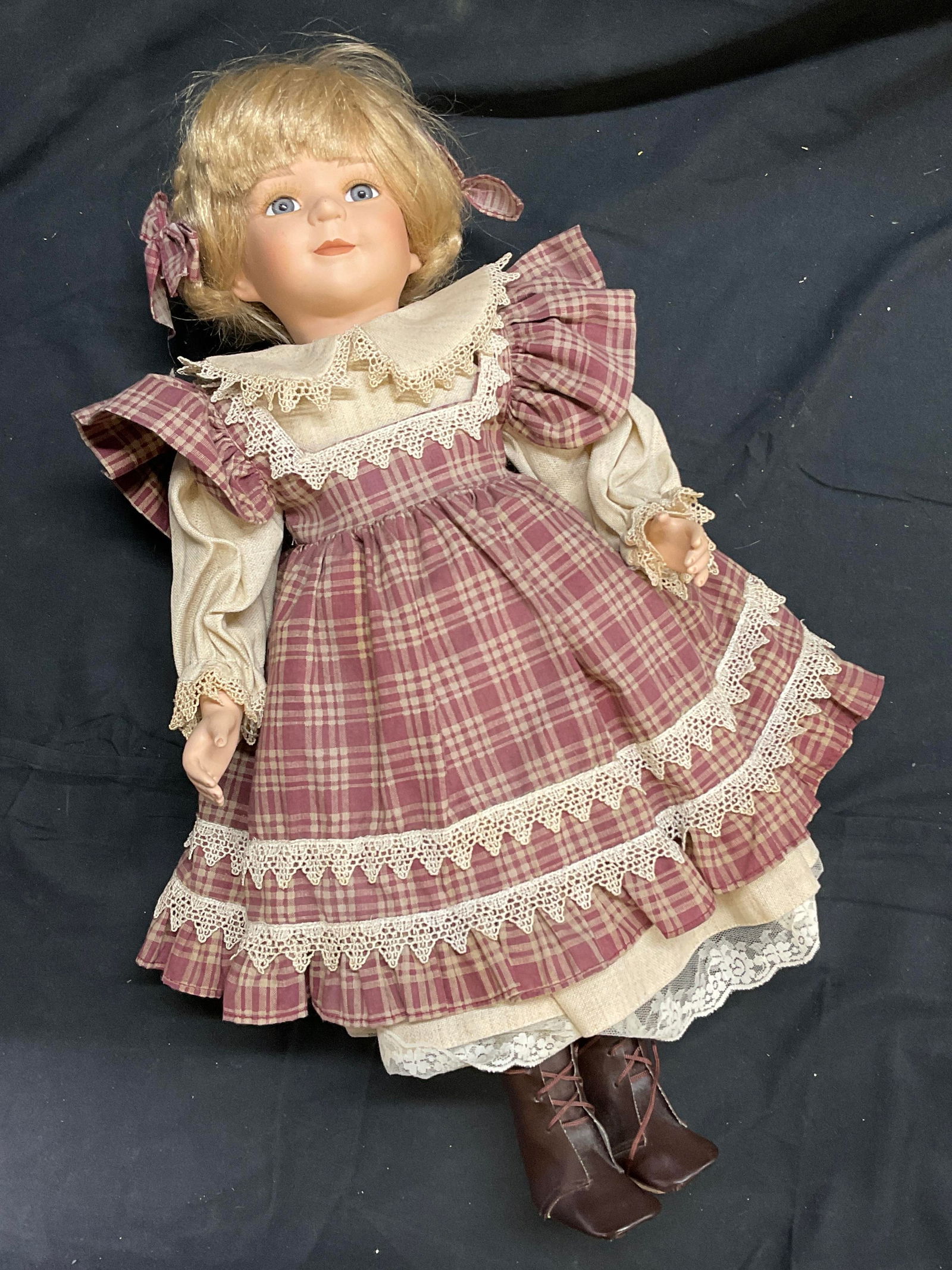 Vintage Porcelain Doll W/ Plaid Dress: A vintage porcelain limb doll wearing a plaid dress. The doll is crafted from porcelain and fabric materials. Measures approx. 21L x 9W in. Surface wear consistent with age, use, and exposure. Hair ap