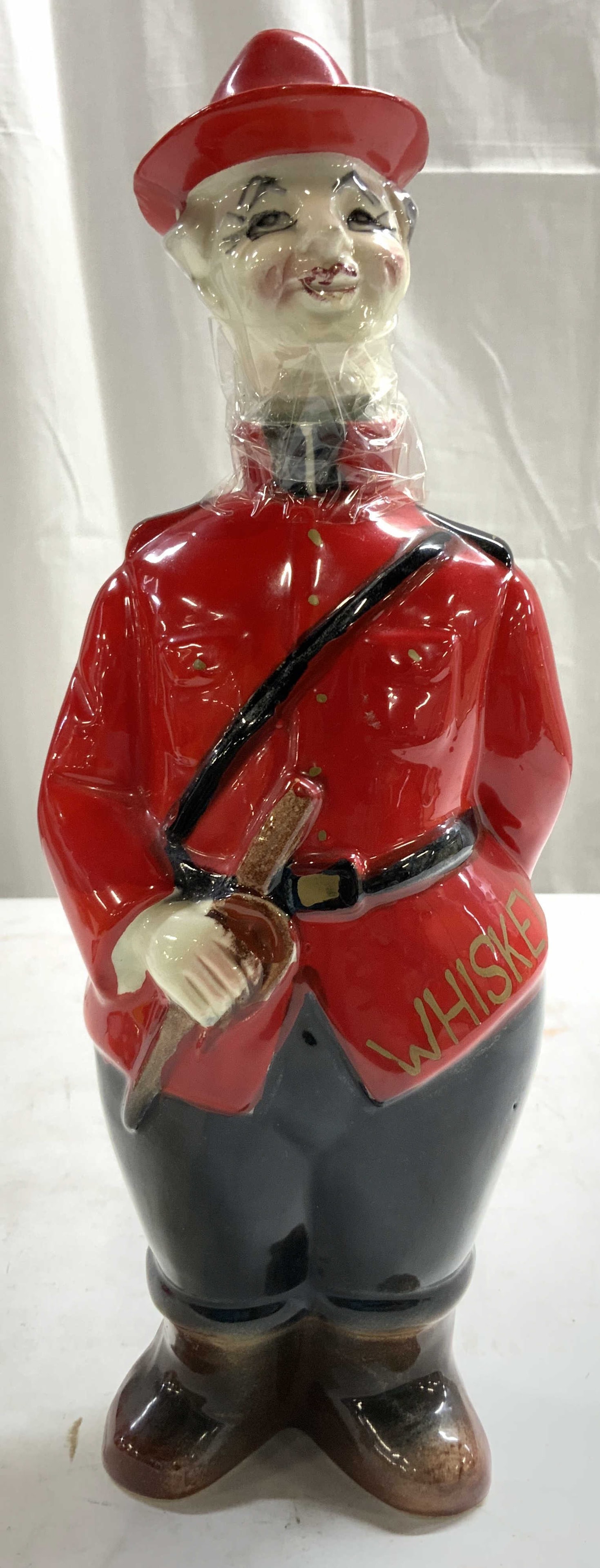 Canadian Mountie Porc Whiskey Decanter W Stopper: Underside has crossed arrow trademark. Decanter has Canadian Mountie form. Piece is red, white and black toned. Decanter includes stopper. Piece measures approximately 12 inches tall 4 inches wide 2.7