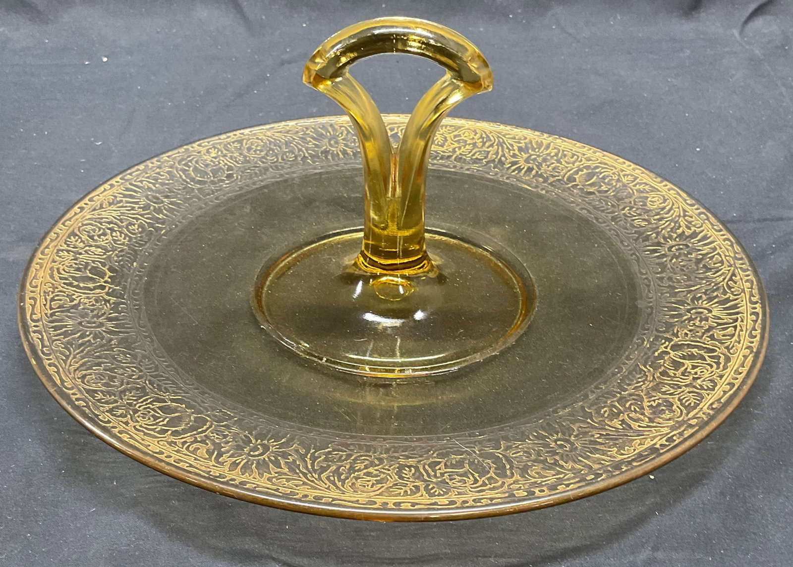 Round Gilt Amber Glass Platter with Handle: Round amber glass platter with handle. Gilt floral pattern rim. Measures approx. 10.25 inches wide. Surface wear including loss to gilt and scratching observed. Platter, platter with handle, glass pla