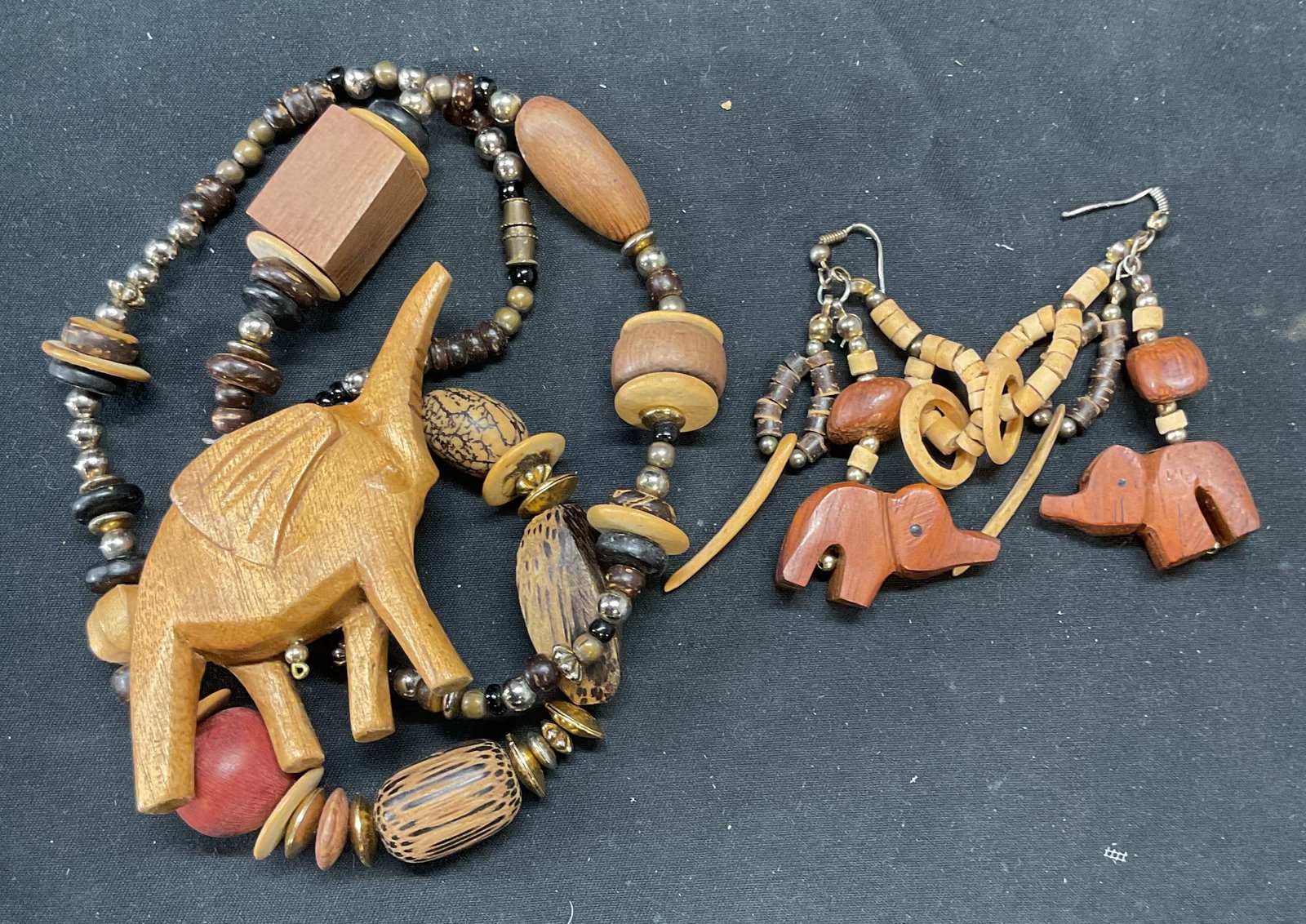 2 Carved Wood Elephant Necklace & Earrings: Lot of 2 vintage jewelry pieces. Carved wooden elephant pendant necklace and dangle earrings. Necklace drop length approx. 10.5 inches. Earrings measure approx. 2 inches long. Bending to earring hooks