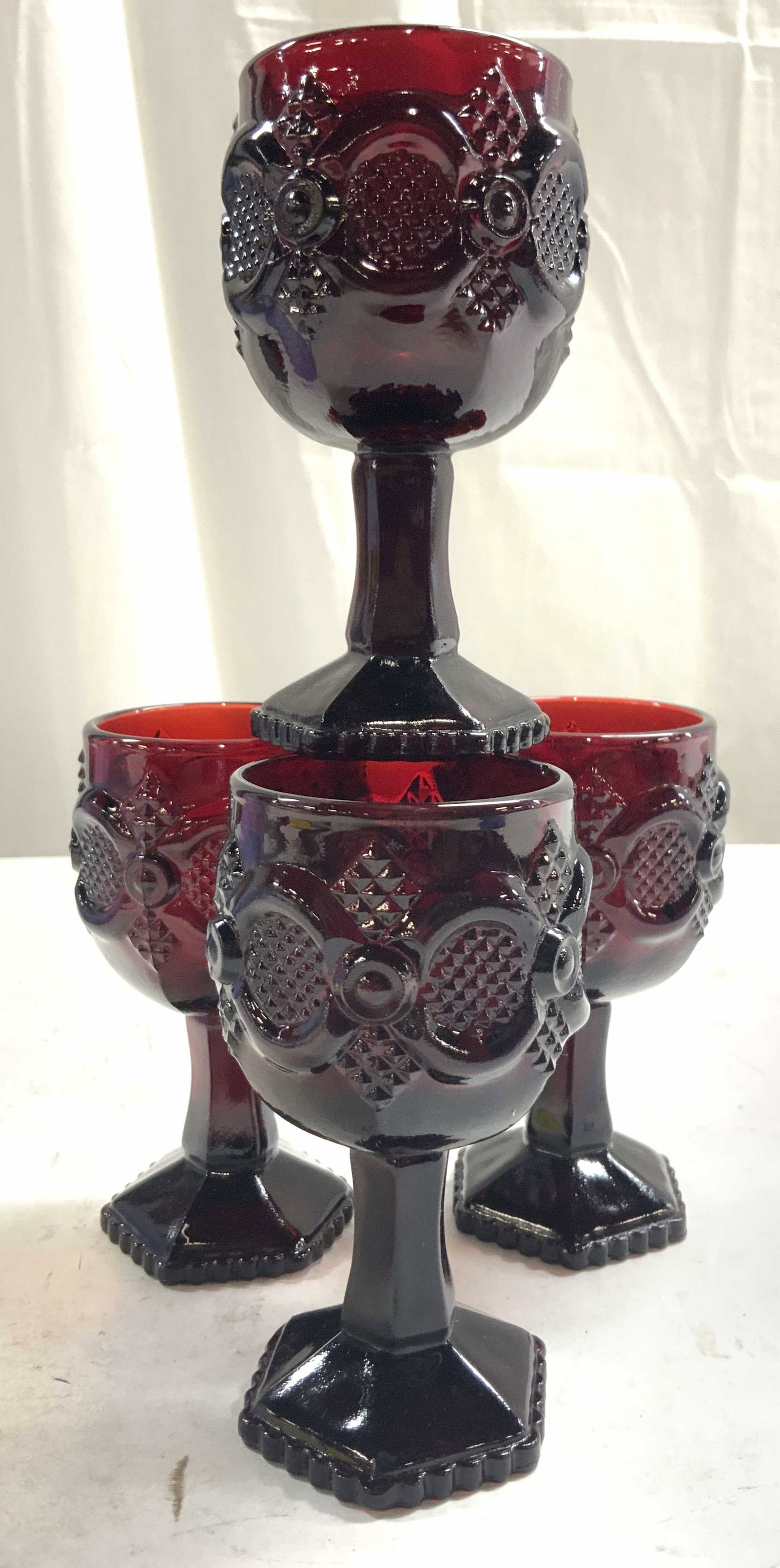 AVON Set 4 Cranberry Cordial Glasses: Undersides read AVON. Lot includes 4 cordial glasses. Each are dark cranberry toned. Pieces each have hexagonal form bases. Each piece has beveled and relief detail. Cordial glasses each measure appro