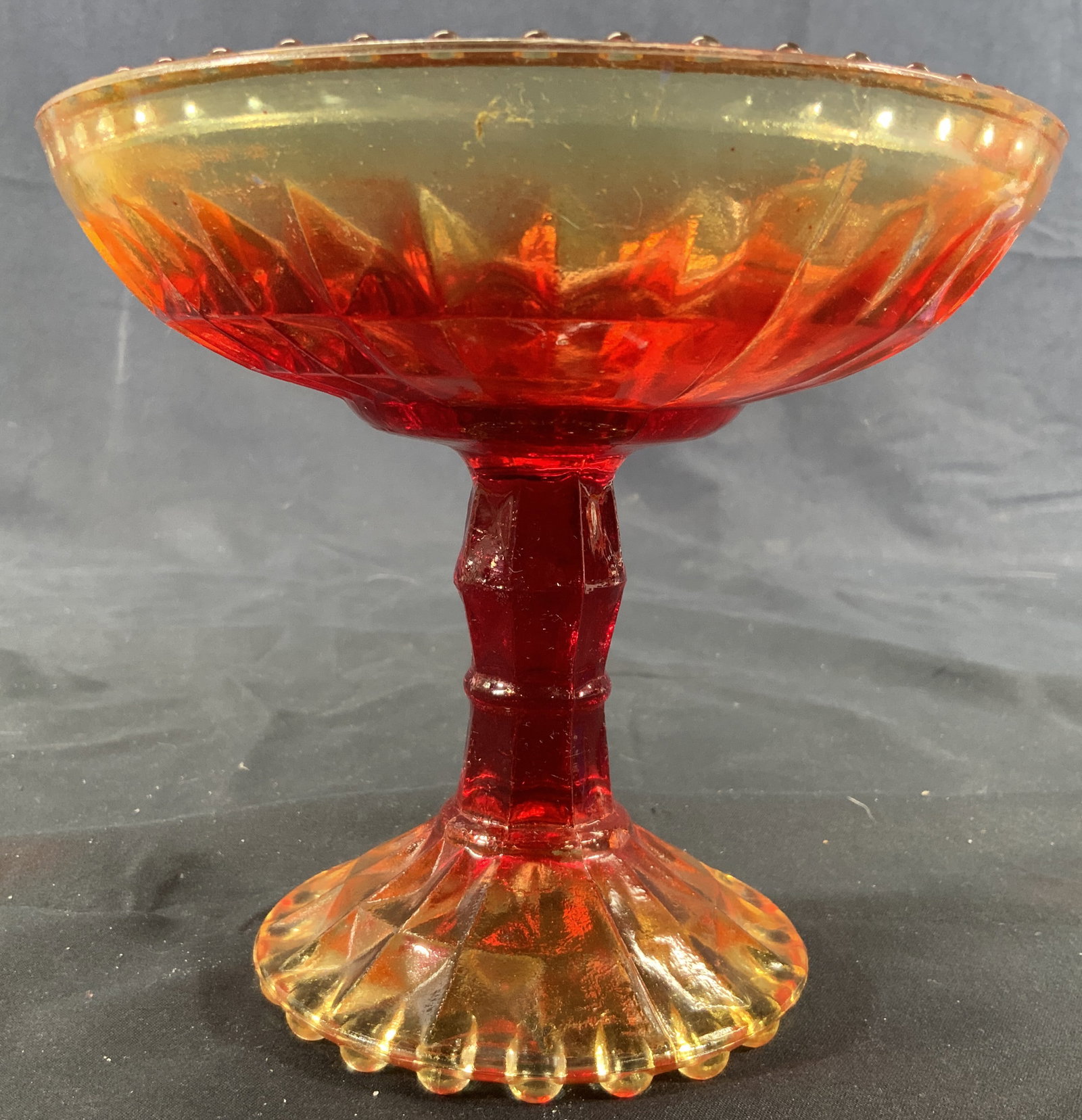Carnival Glass Amberina Pedestal Candy Bowl: Carnival Glass Bowl. Glass is amberina, candy bowl is on a footed pedestal. Vessel has a yellow to red gradient. Top and bottom is studded. Candy bowl measures approx. 6 D x 5.5 H in. Minor wear to am