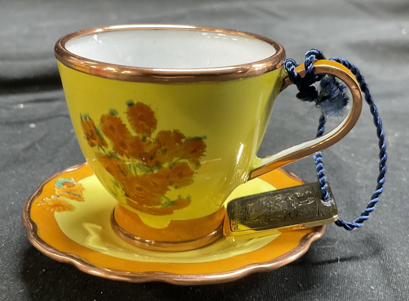 Charlotte Di Vita Mini Porc Cup & Saucer In Box: Underside of lid reads CHARLOTTE DI VITA. Lot includes 1 teacup, 1 saucer, & Original orange toned box. Each piece is yellow and orange toned with floral and leaf detail. Saucer measures approximately