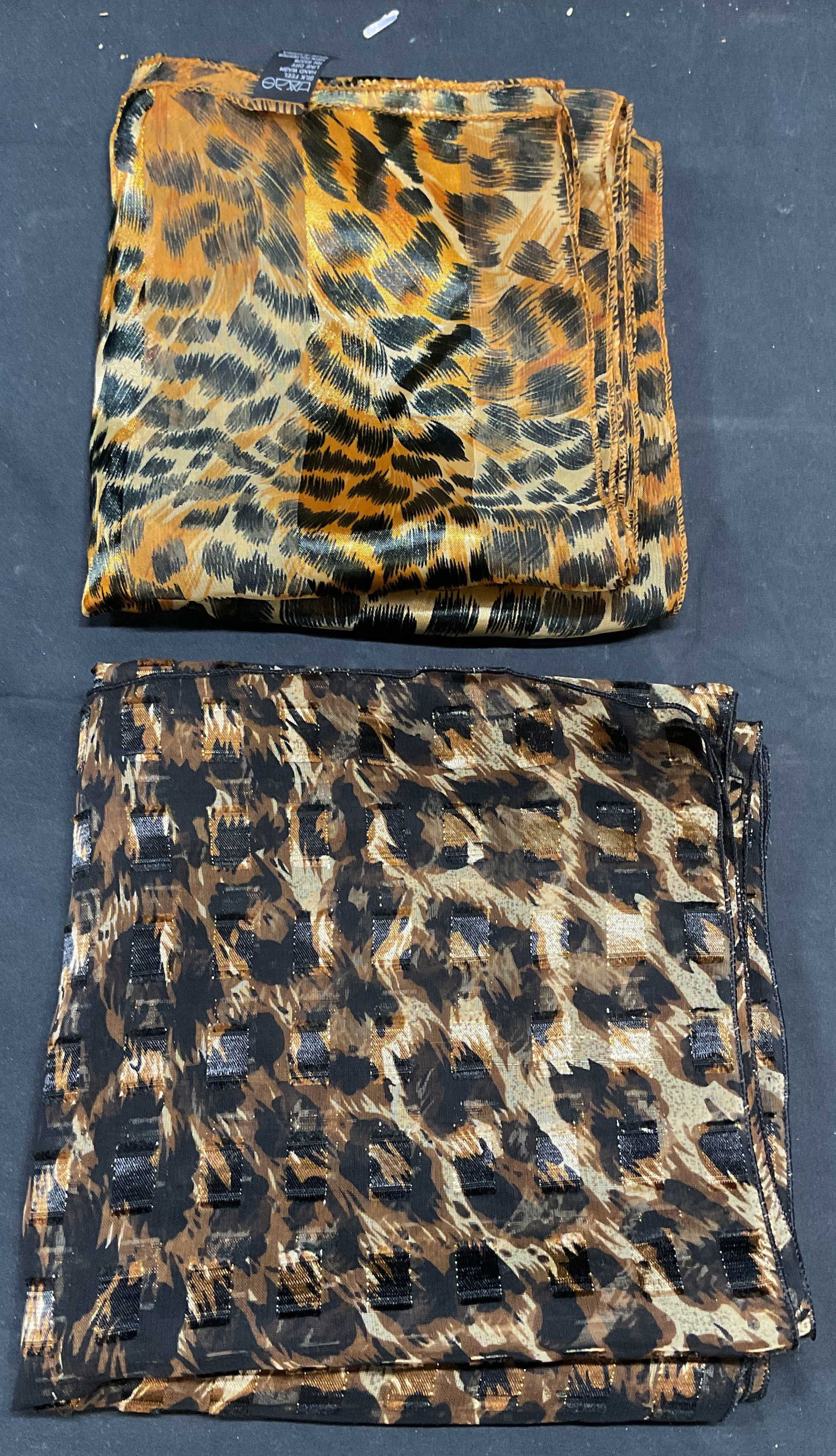Lot 2 Brown & Orange Animal Print Scarves: Lot of 2 brown, orange, and black toned animal print scarves. Synthetic materials. Measure approx. 60 inches long each. Both scarves have some wear to material consistent with exposure. Ladies scarf, 