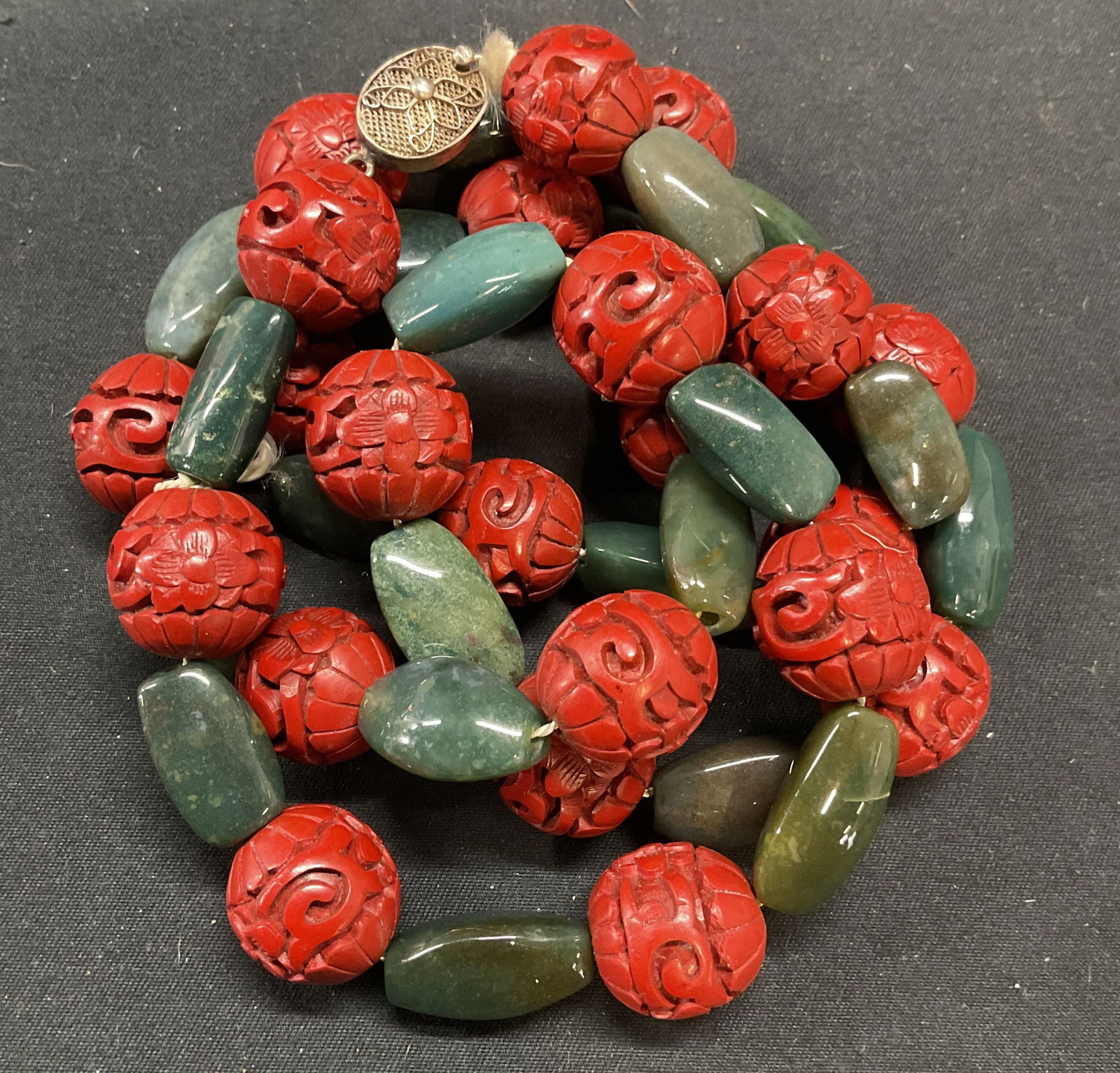 Green Semiprecious & Cinnabar Lacquer Necklace: Vintage green semiprecious gemstone and carved cinnabar lacquerware beaded necklace with decorative silver clasp. Marked silver. Drop length approx. 15 inches. Some surface wear including scratching o