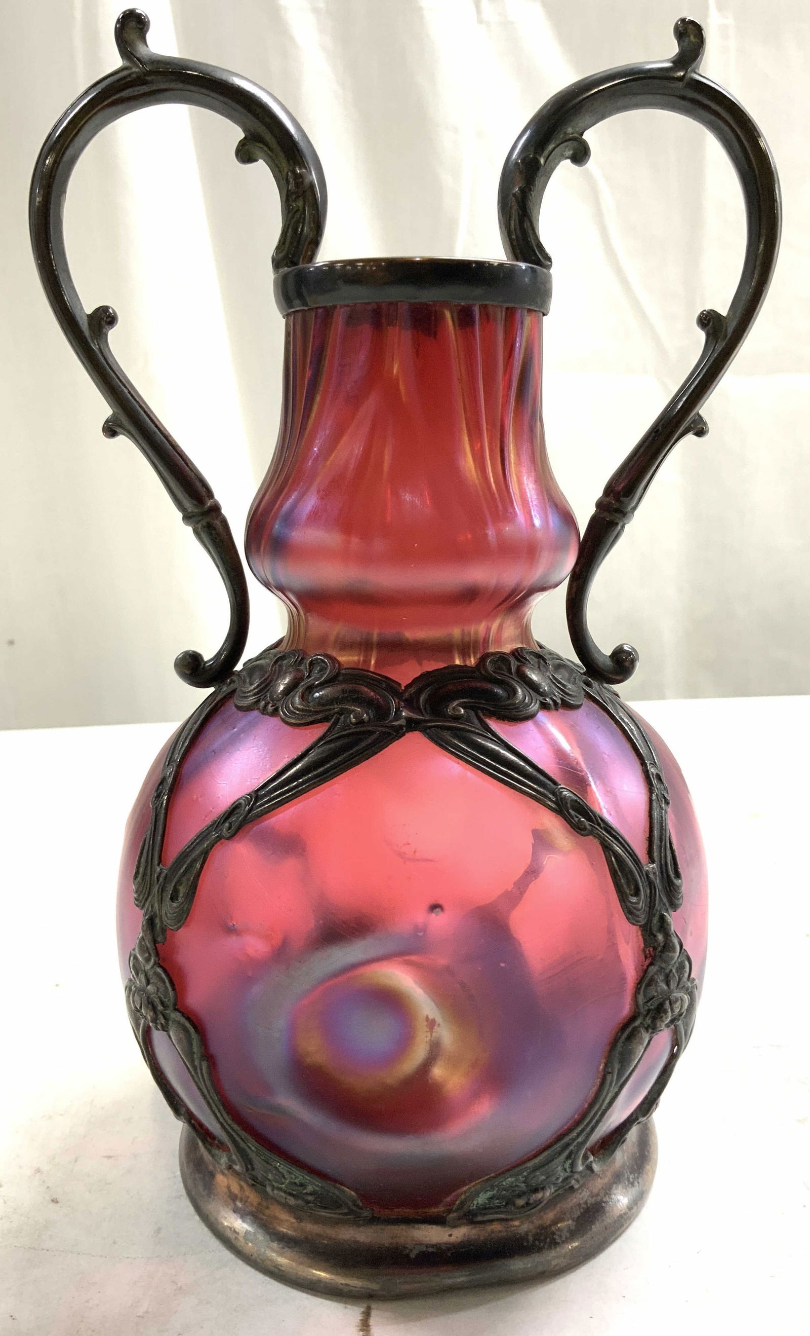 JOH. LOETZ WIDOW Apollo Quad Pl Art Nouveau Gls Vs: JOHAN LOETZ WIDOW. Underside inscribed APOLLO SILVER CO QUADRUPLE PLATED. Art nouveau vase with cranberry toned glass vessel & quadruple plated overlay. Vase has scrolled handles. Vase measures approx