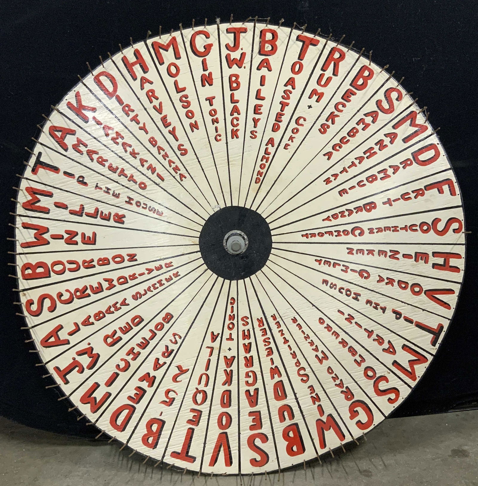 Alcoholic Drinks Game Wheel Bar Decor 3ft: Wooden game wheel with nails in border and bolt in center hole. Game wheel has slivers of options of drinks or shots that can be landed on. Some include Baileys, Vodka Gimlet, Bourbon, Harveys, Tequil