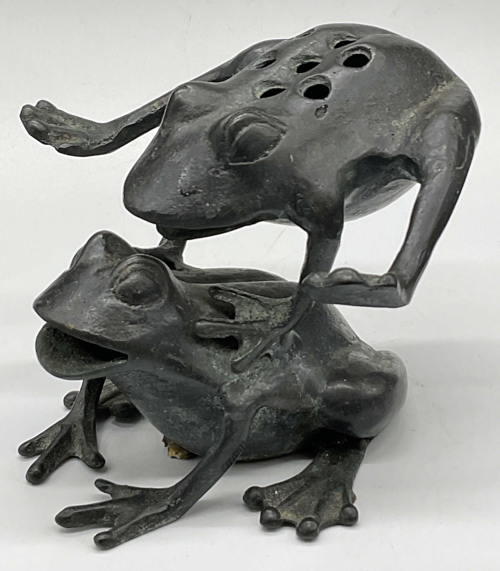 Bronze Leaping Frog Figural Flower Frog Sculpture: Bronze Leaping Frog Figural Flower Frog. The sculpture depicts two frogs playing leap frog . Pierced metalwork to the top. Measures approx. 4H x 5D x 6W in. Patina. Residue to underside. Surface wear 
