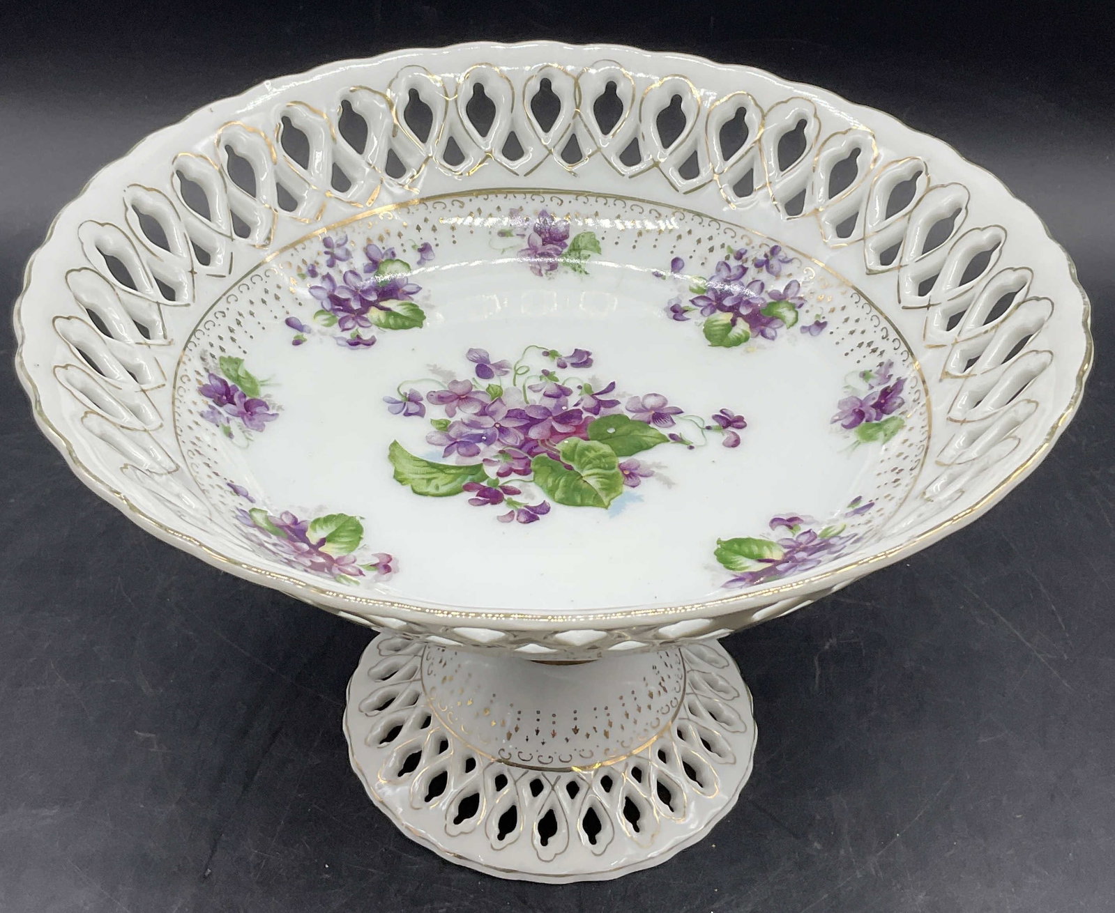 Floral Violet Motif Porcelain Pedestal Dish: Floral Violet Motif Porcelain Pedestal Dish. Pierced or lattice style design to the rim and base. Gilt line work. Measures approx. 5.75H x 9W in. Loose piece to interior. Repair present. Cracking and 