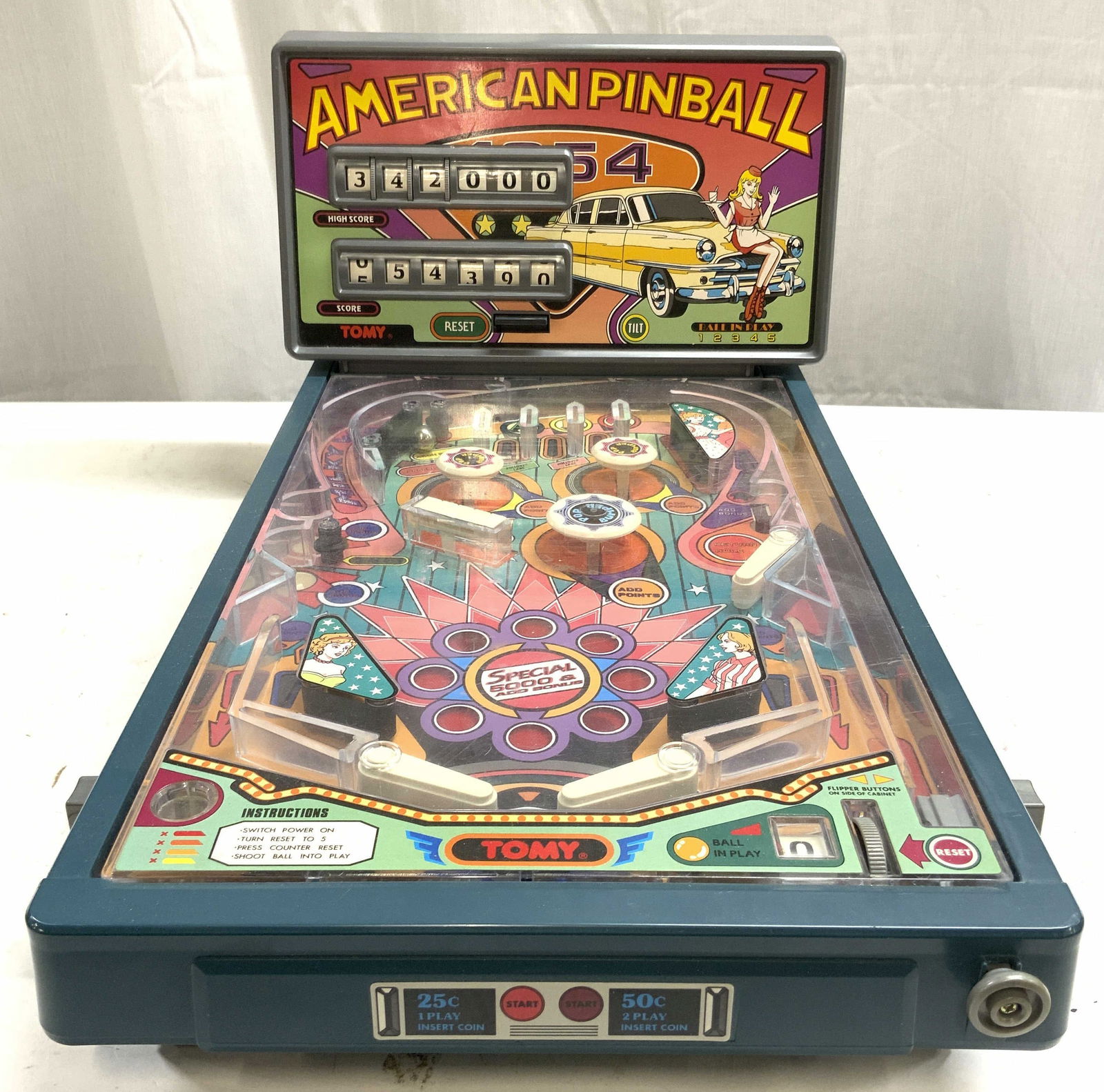 TOMY Vintage Portable Pinball Machine: Pinball machine is trademarked TOMY. Piece is vintage. Machine is footed. Piece is plastic. Scoreboard reads AMERICAN PINBALL depicts a diner waitress wearing roller skates sitting on a car. Measures