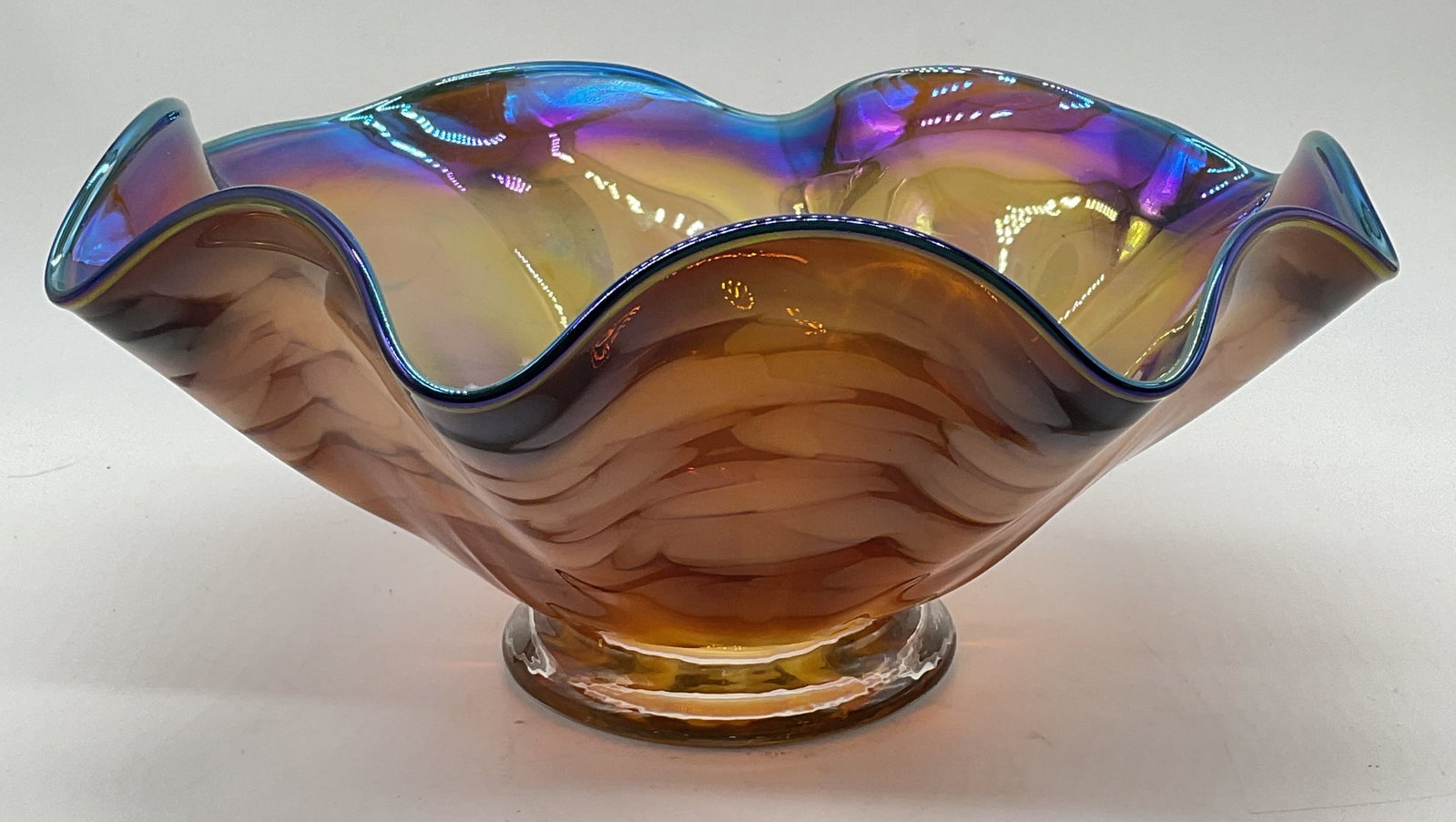 Metropolitan Museum Art Handkerchief Glass Bowl: Metropolitan Museum of Art handkerchief rim glass bowl. Iridescent interior and swirled amber toned exterior with blue rim. Signed MMA Glass on underside. Measures approx. 11 x 5 inches. Piece has wei