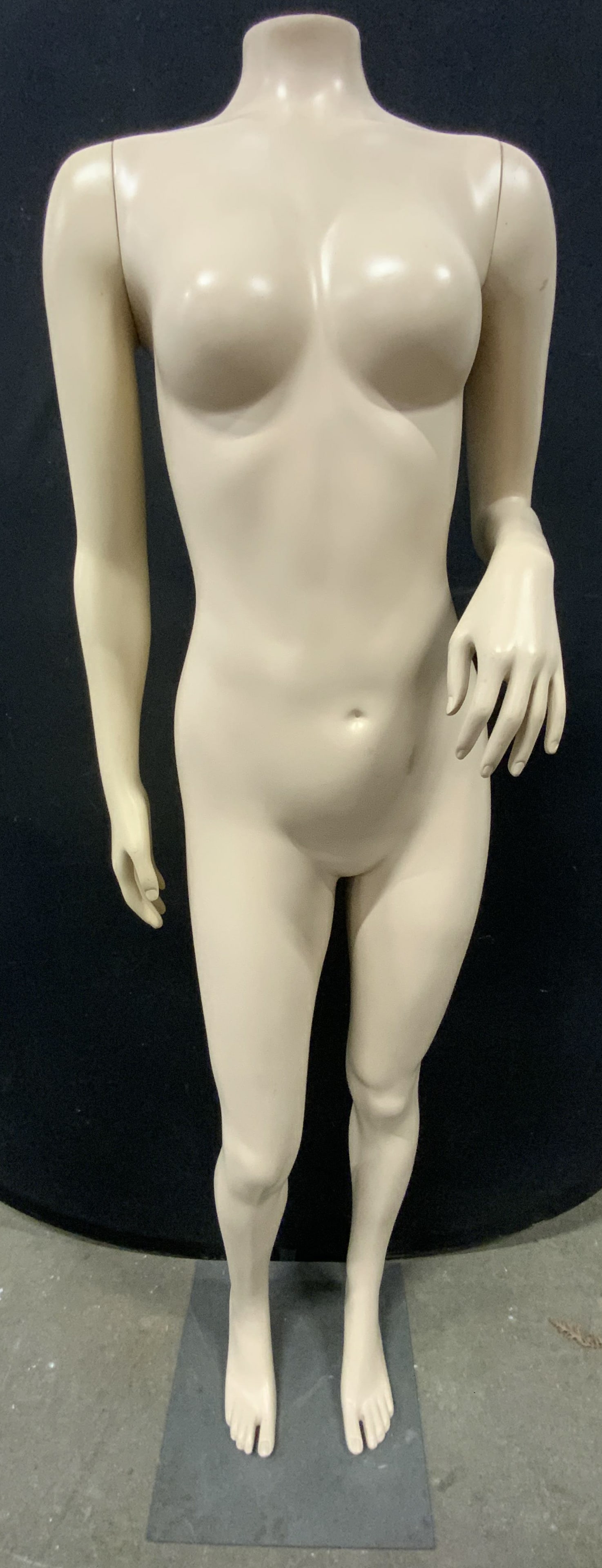 Female Nude Figure Headless Fiberglass Mannequin: Mannequin appears to be fiberglass. Piece is tan toned. Female nude Mannequin with slate toned metal base. Mannequin has 1 bent & 1 straight arm. Piece is headless. Mannequin measures approximately 60
