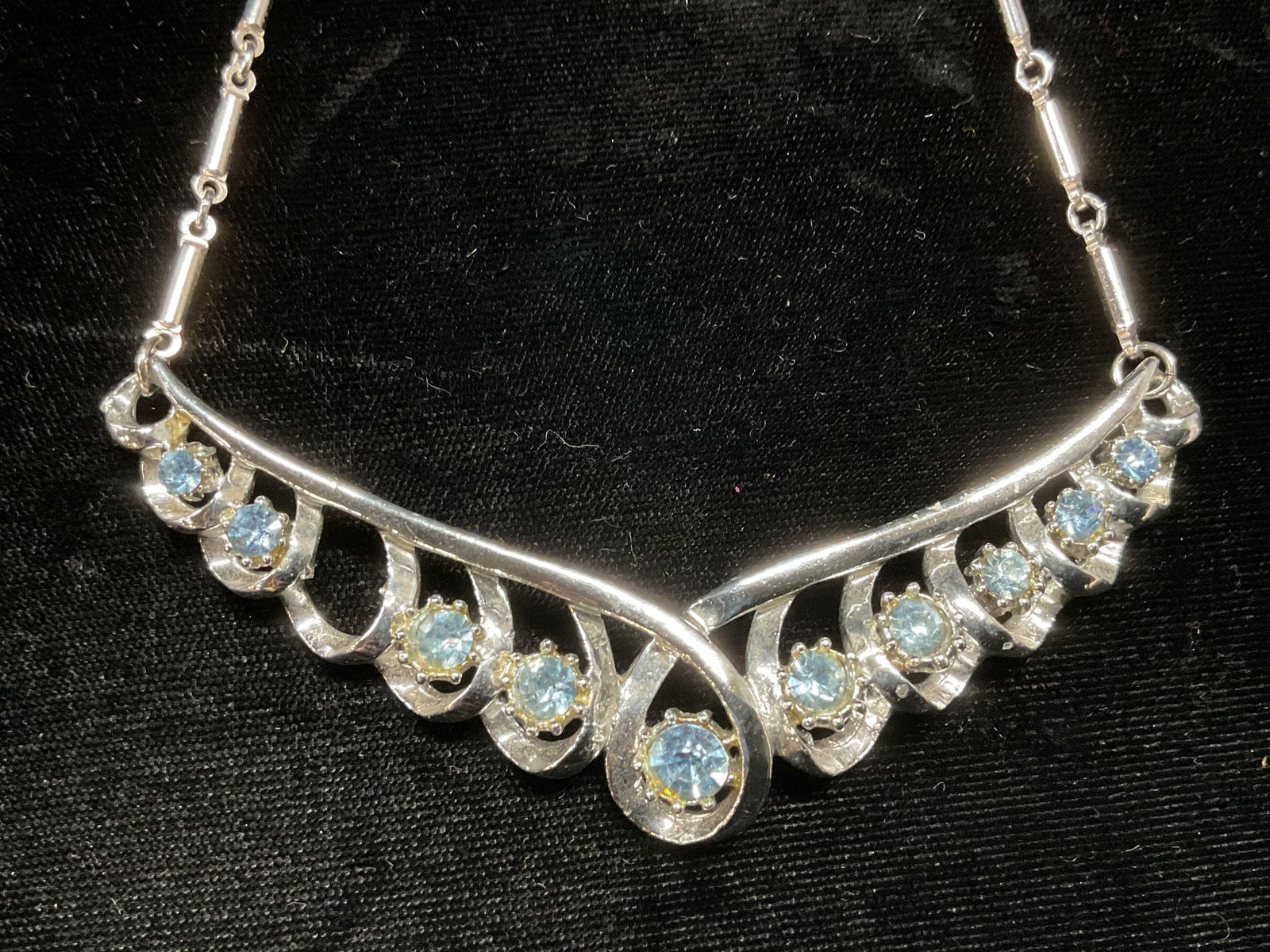Vtg Coro Silver Tone Blue Crystal Necklace: Vintage Coro silver tone necklace with blue crystal decorated pendant. Signed on pendant. Additional mark illegible. Drop length approx. 6.75 inches. One piece needs repair. Some scratching observed.