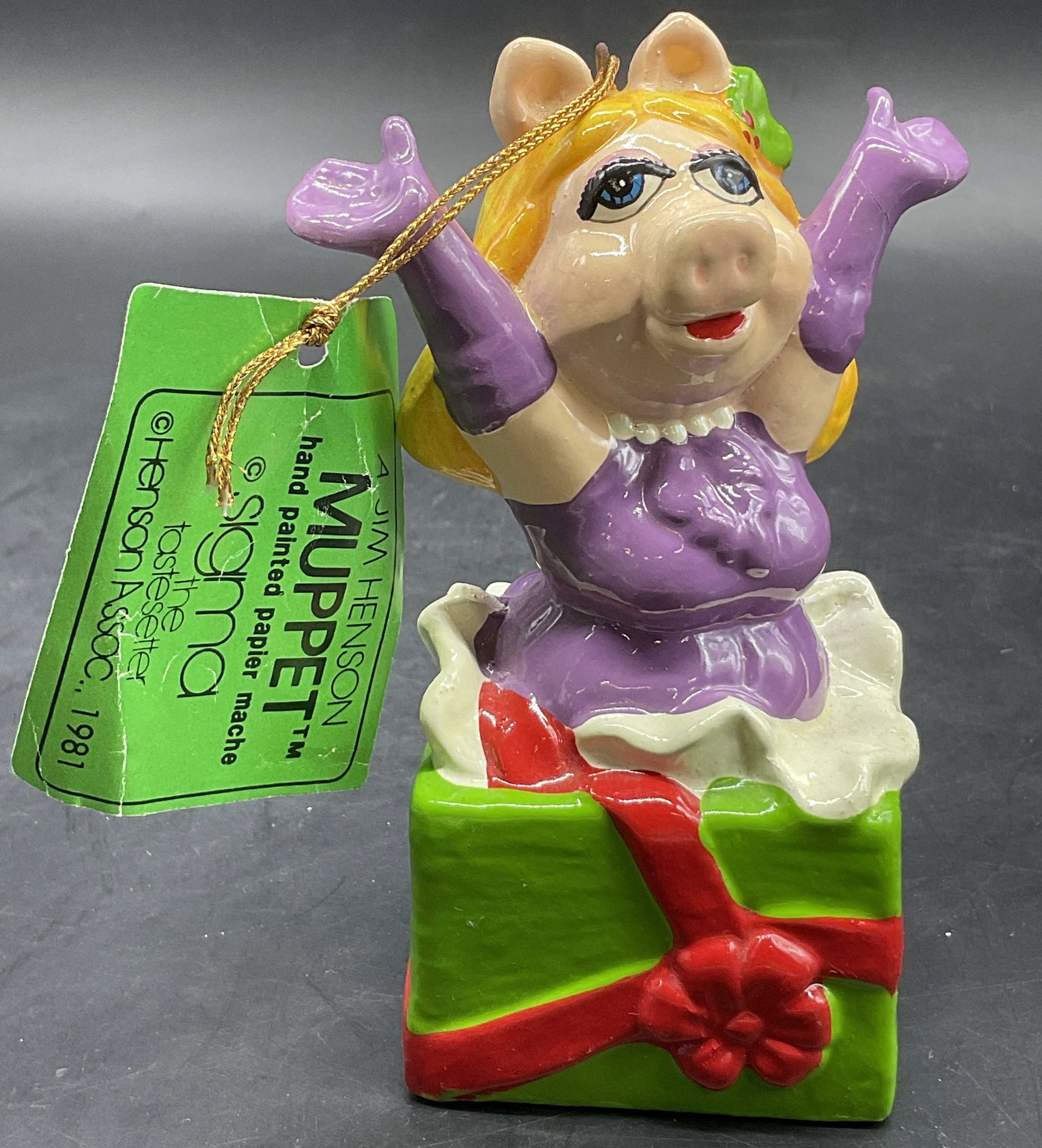 1981 HENSON ASSOC. Sigma Ms. Piggy Figural, OrgTag: A 1981 Jim Henson Muppet HENSON ASSOC. Sigma Ms. Piggy Papier Mache Figural. Ms. Piggy is depicted bursting from a gift. Original tag attached. Measures approx. 5H x 3W in. Surface wear consistent wit
