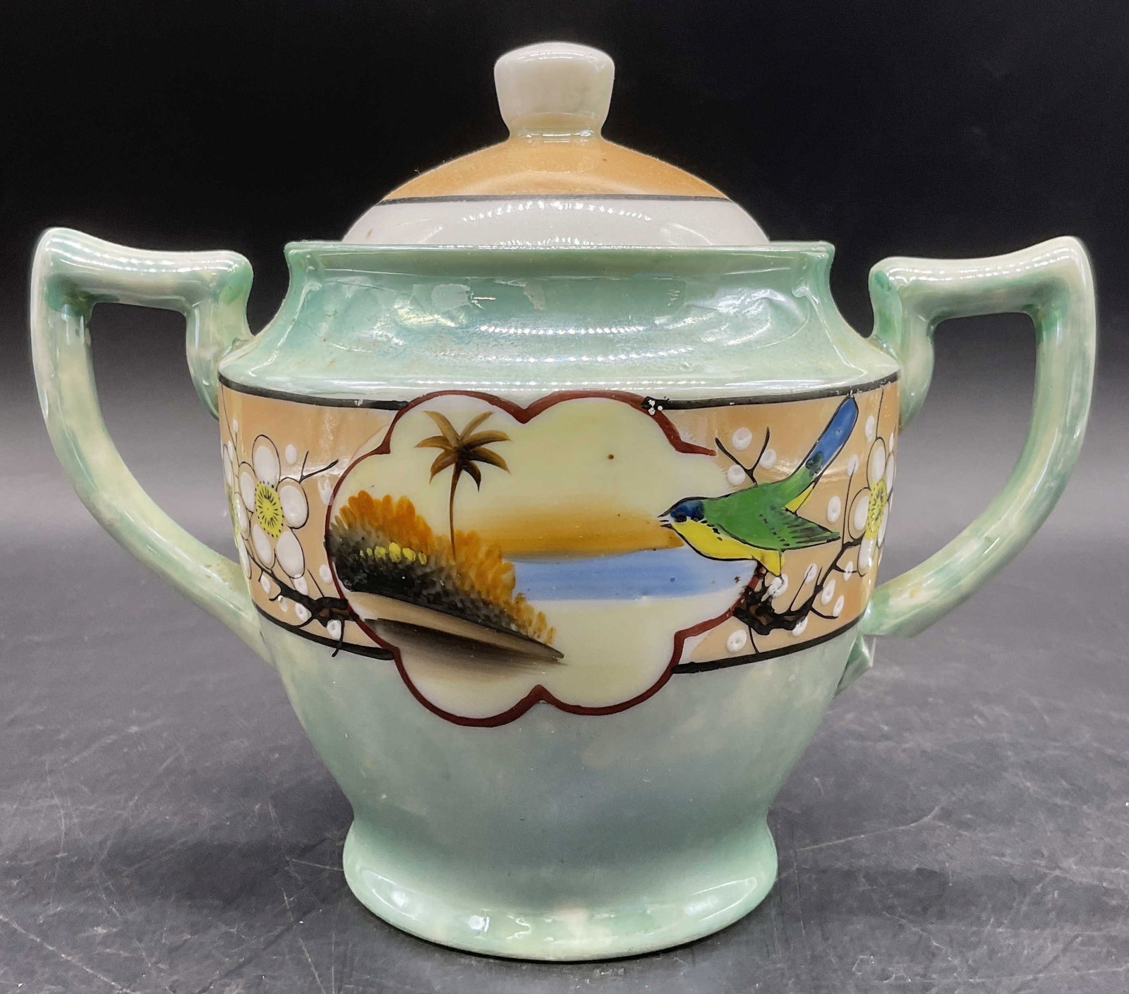 Trademarked Hand Paint Lusterware Sugar Bowl, Lid: A hand painted lusterware porcelain sugar bowl. Handles on either side. Lidded. Underside is trademarked and reads HAND PAINTED. Measures approx. 5.5H x 6.5W in. Surface wear and wear to finish presen