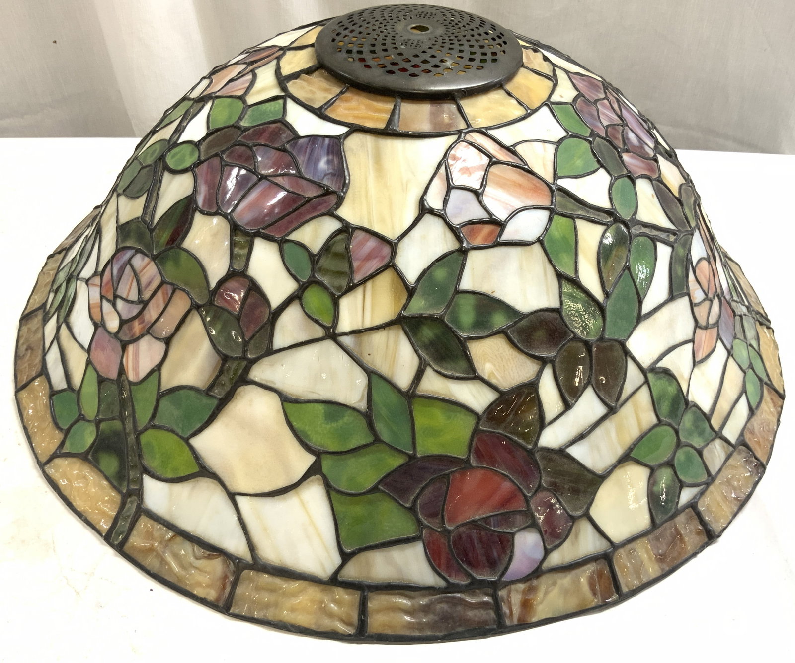 Tiffany Style Stained Glass Lamp Shade: Lamp shade is stained glass. Piece has Tiffany style. Shade has multi toned floral and leaf detail. Top of piece has metal area with pierced detail. Lamp shade measures approximately 21.5 inches wide 