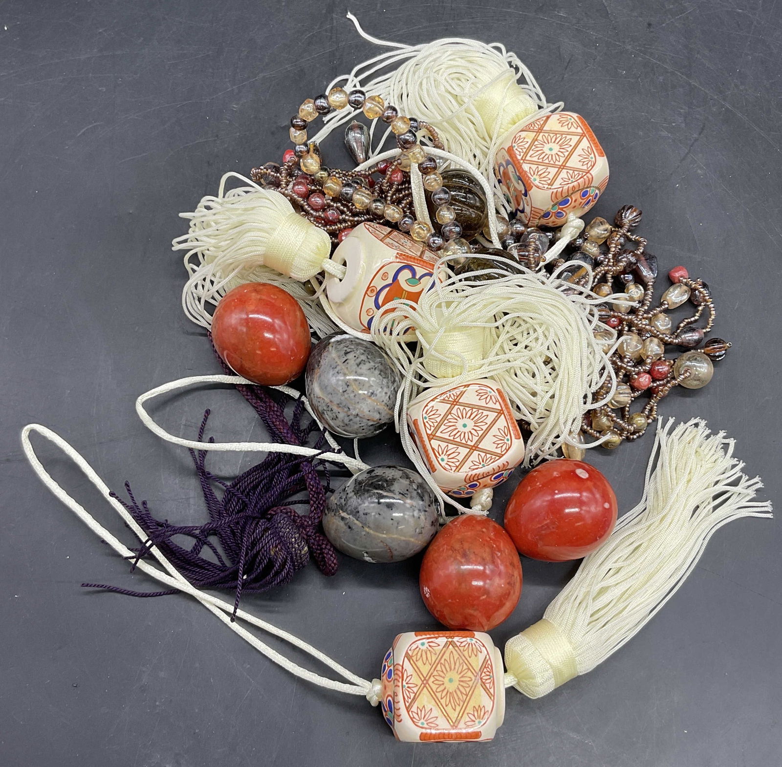 Group Lot Ceramic & Fabric Tassels + Beads: A group lot of ceramic and fabric tassels & beads. The pieces are multicolored. Some beads are crafted from stone and others are glass or plastic. Tassels measure approx. 12.5L x 1.25W in. Surface wea
