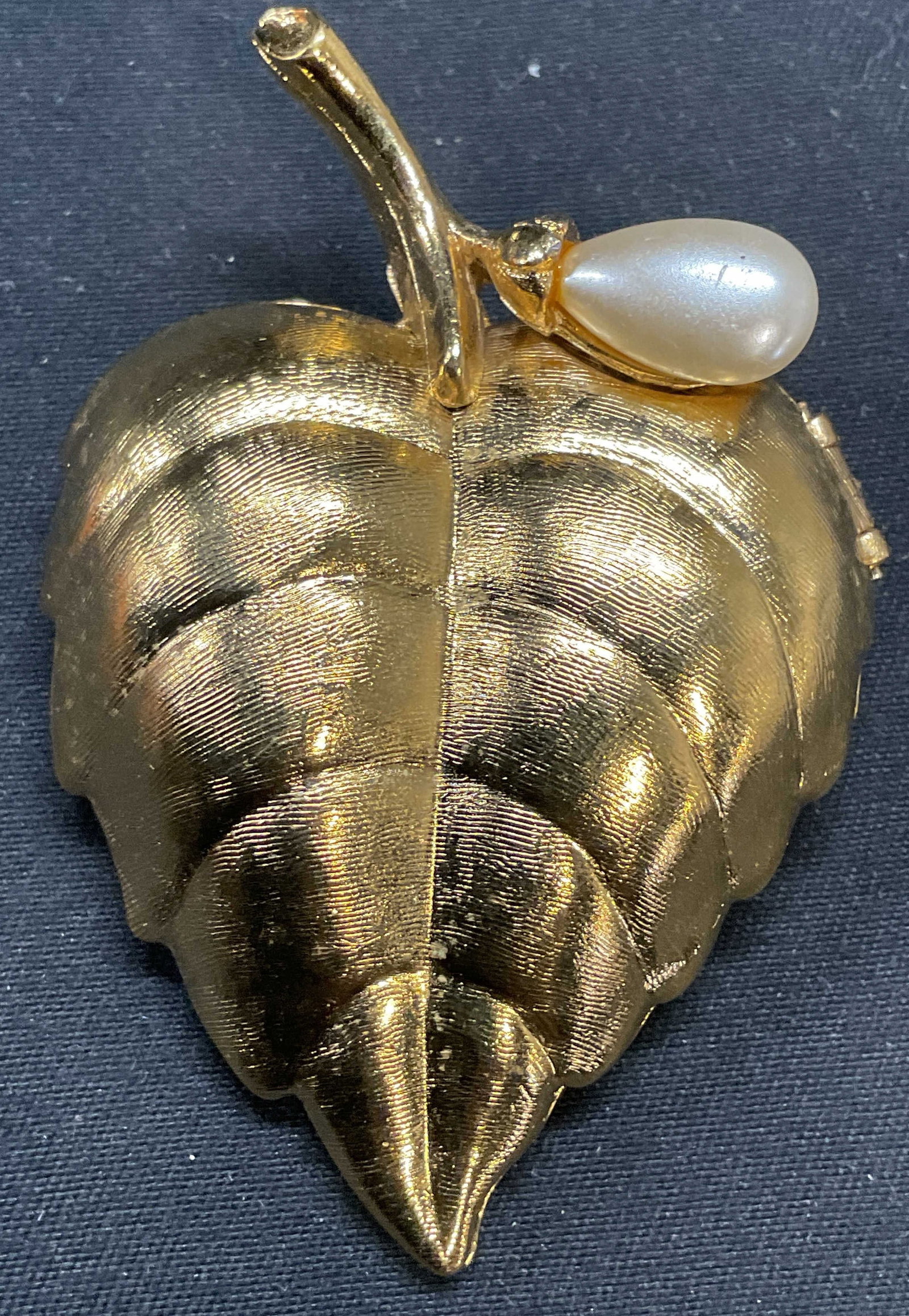 Vintage Avon Gold Tone Leaf Locket Brooch: Vintage Avon gold tone leaf locket brooch with faux pearl decoration. Signed on interior. Hinge pin on underside. Measures approx. 2.25 x 1.5 inches. Some surface wear including scratching observed. J