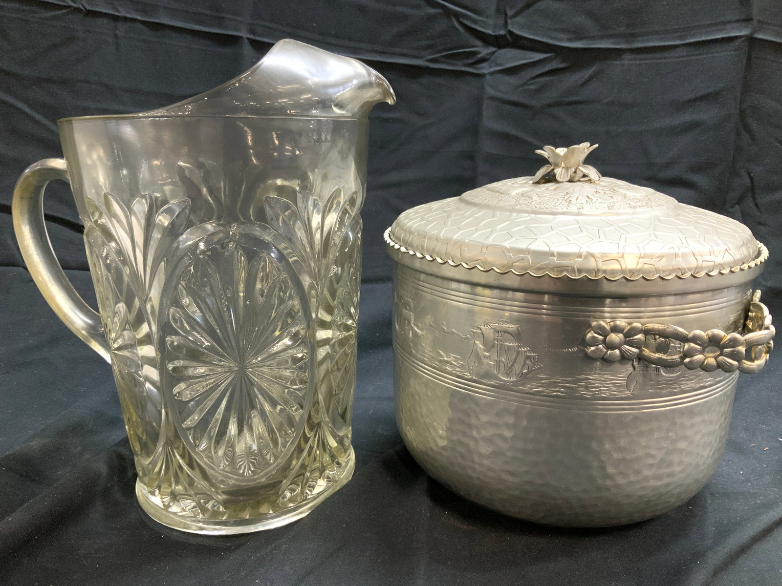 Lot 2 FORMAN FAMILY Ice Bucket & Glass Pitcher: Lot includes 1 silver toned metal ice bucket with lid, floral detailed handles ship detail, and 1 art glass pitcher with geometric relief detail. Pitcher measures approximately 9.25 inches tall 8 inch