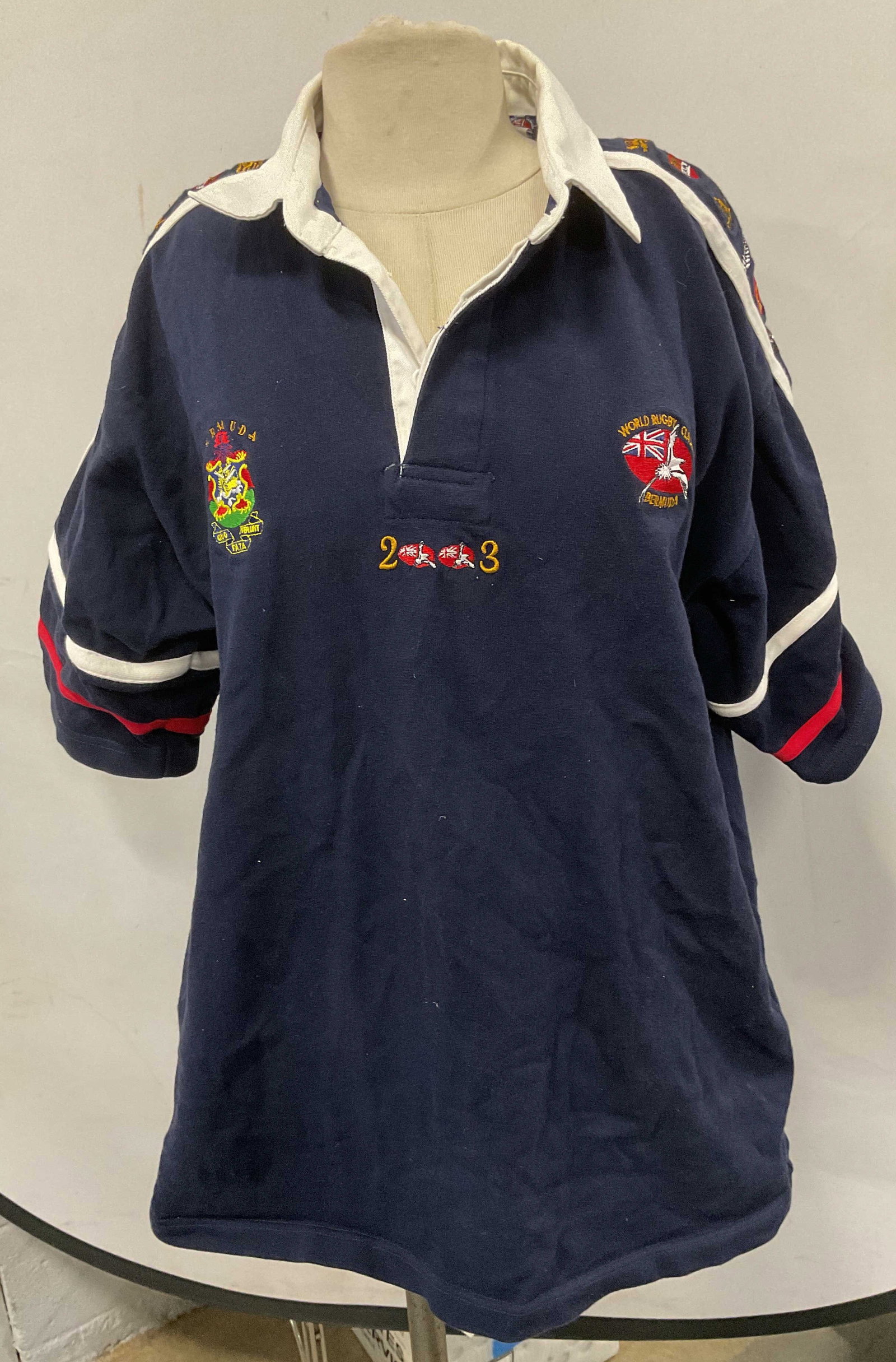 World Rugby Classic Bermuda Blue Shirt: World Rugby Classic Bermuda 2003 blue rugby shirt. Embroidered detail. Size large. 100% cotton. Some wear to material including blemishes consistent with exposure. World rugby classic, rugby shirt, bl