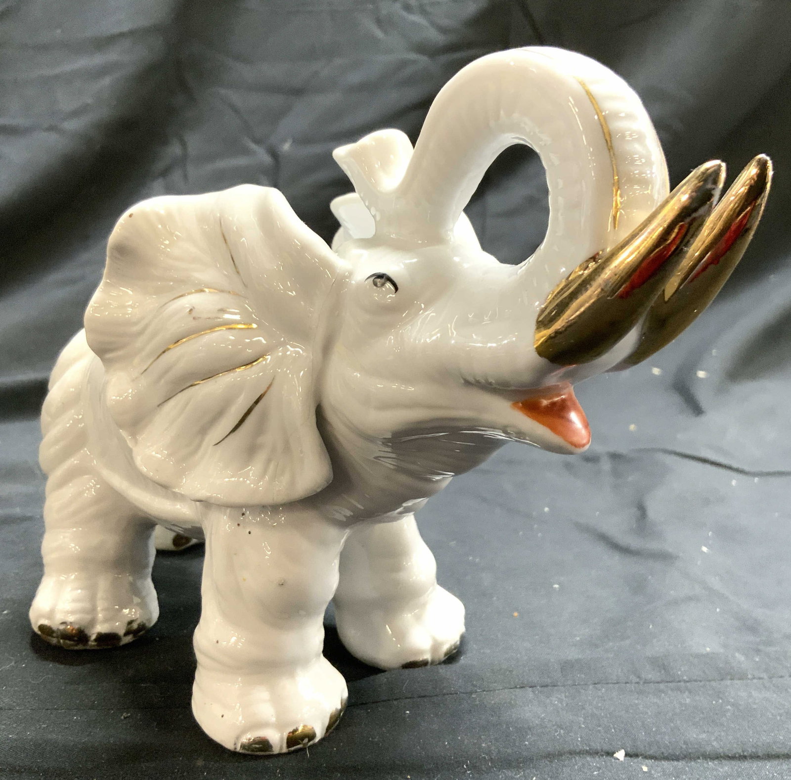 Vintage Asian Porcelain Elephant Figure: Underside is signed with red toned Asian characters. Elephant figure is white toned and porcelain. Piece has gilt detailed tusks. Elephant is depicted with trunk raised. Elephant measures approximatel