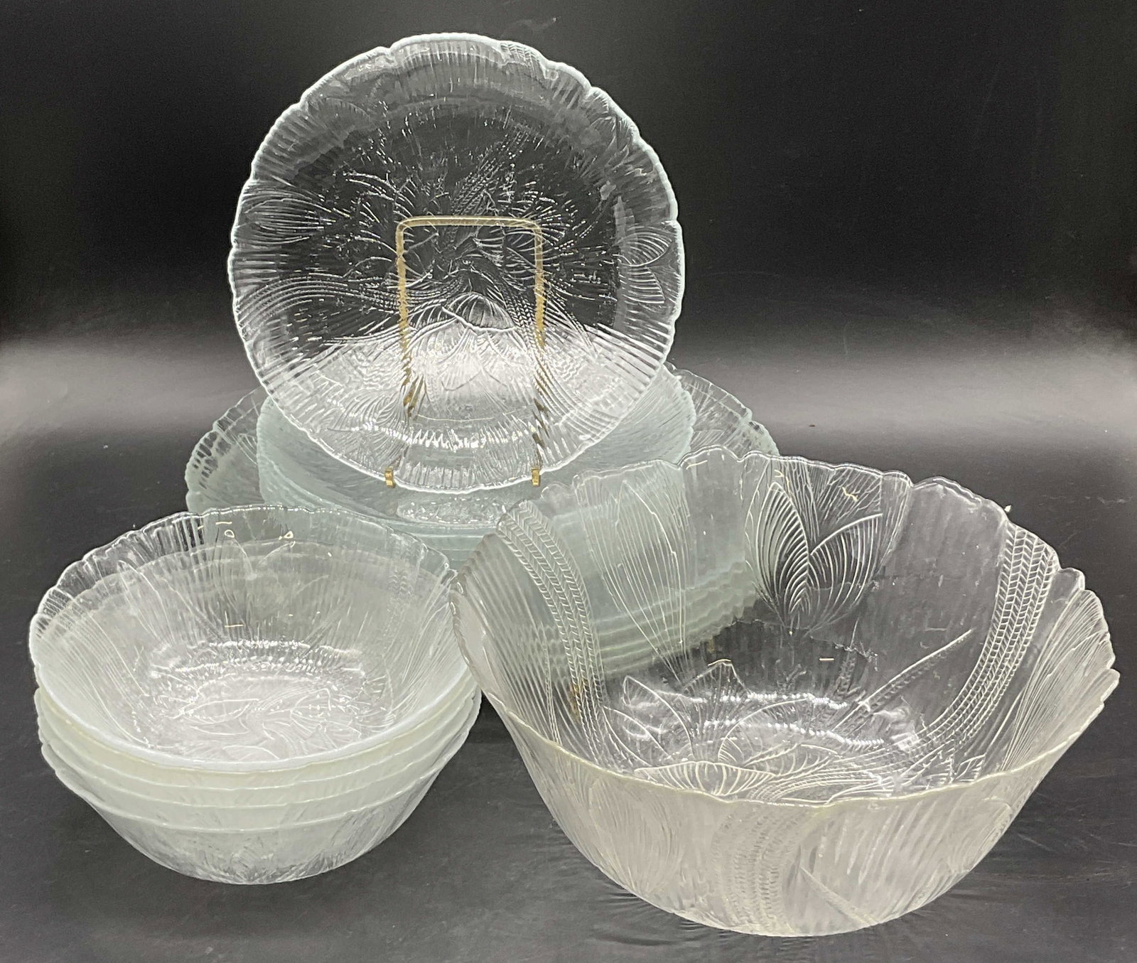 Set 19 Foliage Motif Glass Dinnerware: A set of nineteen clear glass foliage motif dinnerware. Set includes plates and bowls. Largest bowl measures approx. 4H x 9.5W in. Surface wear consistent with age, use, and exposure. Discoloration pr
