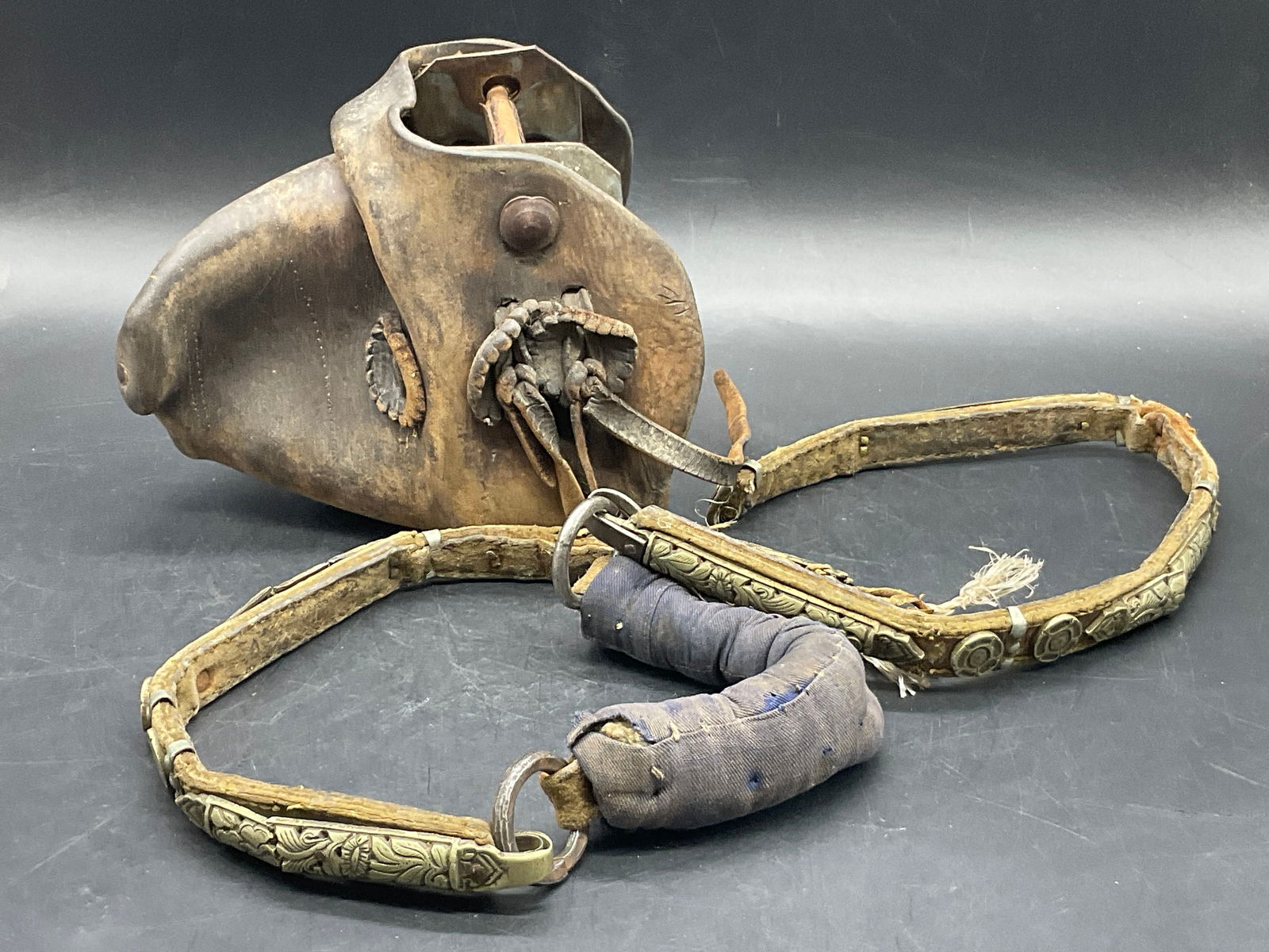 Lot 2 Leather & Metal Decoration Stirrup + Bridle: A stirrup and bridle crafted from leather, fabric, and metal materials. Bridle has metal floral motif decoration. Stirrup measures approx. 6H x 7W in. Measured at widest point. Losses, surface wear, f