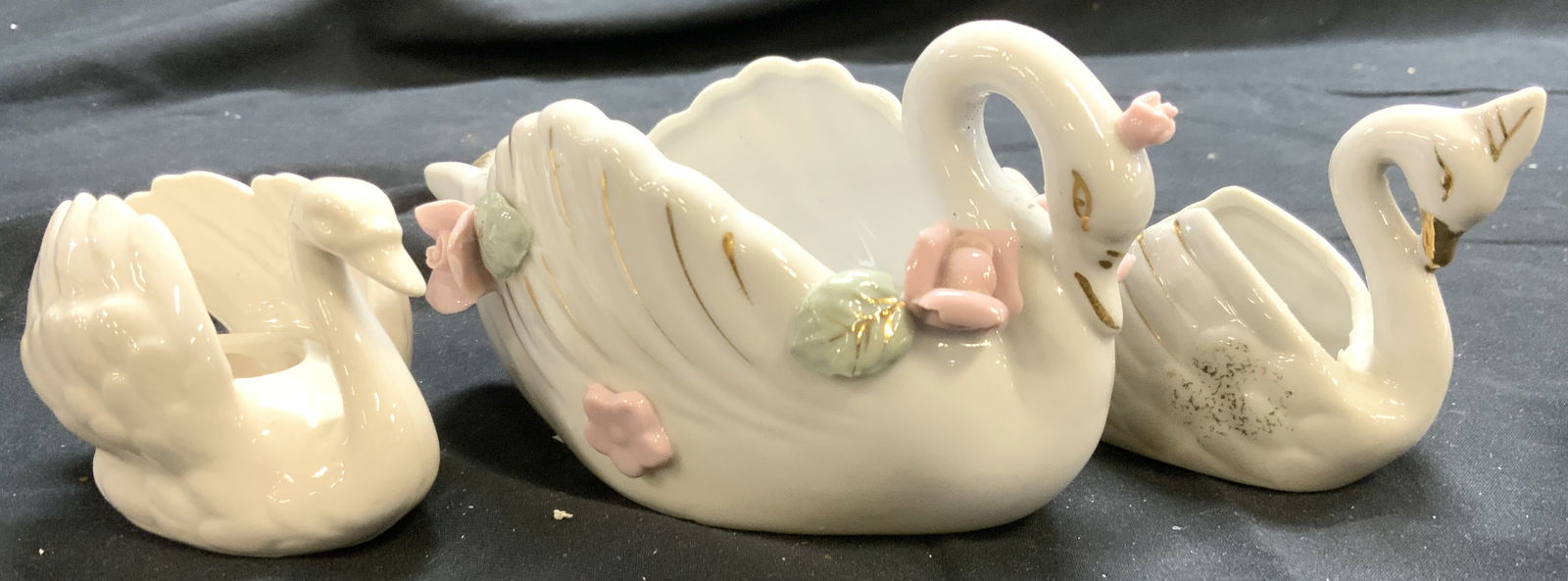 Lot 3 Porcelain Swan Vessels GOEBEL & More: Undersides of 2 are marked JAPAN. Underside of 1 is marked GOEBEL W GERMANY. Largest piece has pink and green toned floral and leaf detail. Two pieces have areas of gilt detail. Largest piece measures