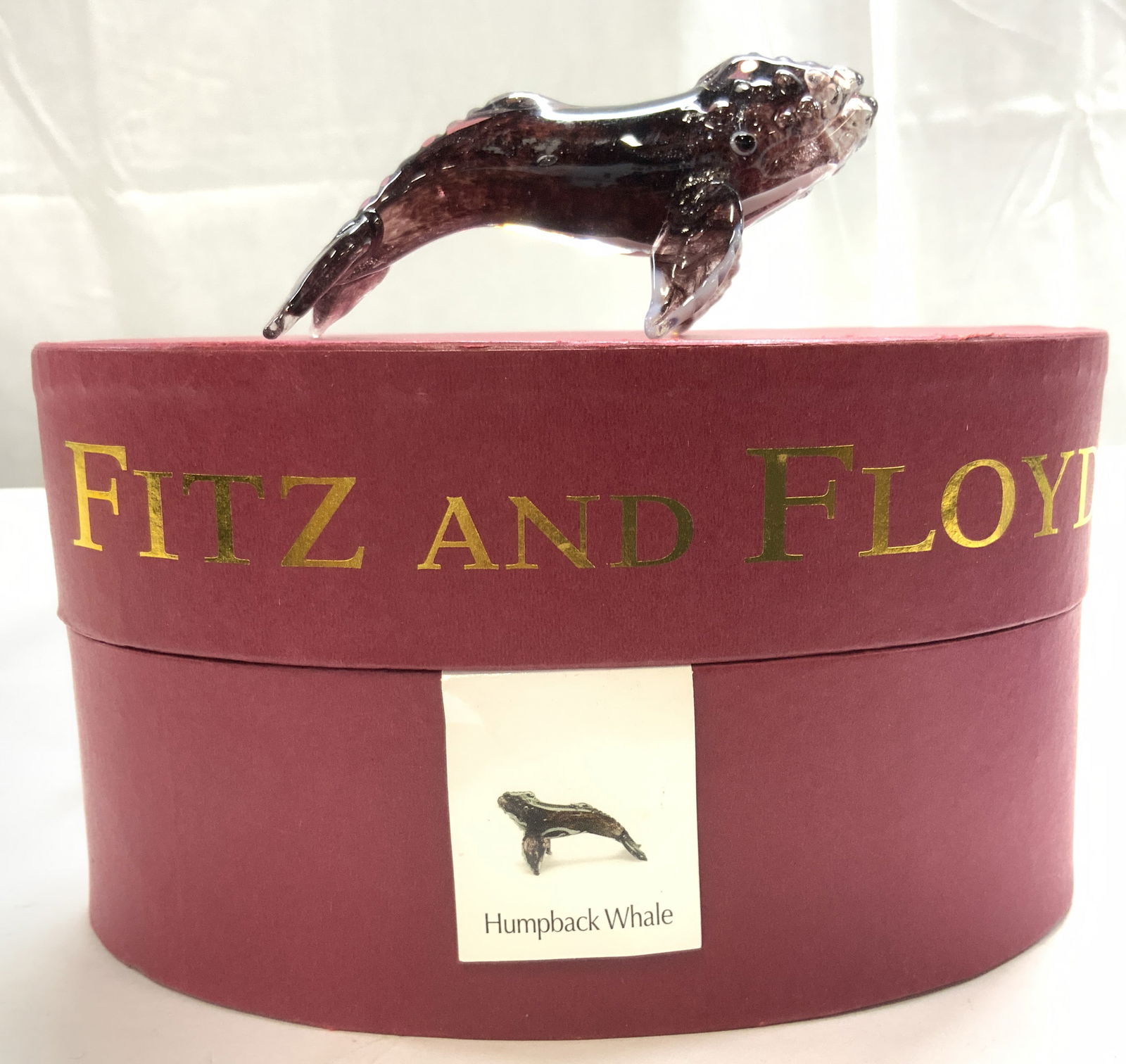 FITZ & FLOYD Gls Humpback Whale Fig w Box: Box reads FITZ & FLOYD. Tag reads HUMPBACK WHALE. Piece includes original box with lid. Box is red with gold toned lettering. Piece has oval form. Humpback whale figure is plum and white toned & has F