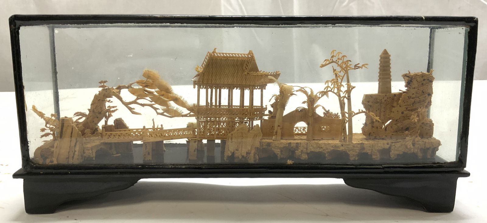 Hand Carved Cork Chinese Pagoda Diorama W Case: Diorama is hand carved cork. Piece is tan toned. Diorama is in the form of a landscape with Chinese pagoda. Piece has black toned case with glass windows. Piece measures approximately 9.25 inches long