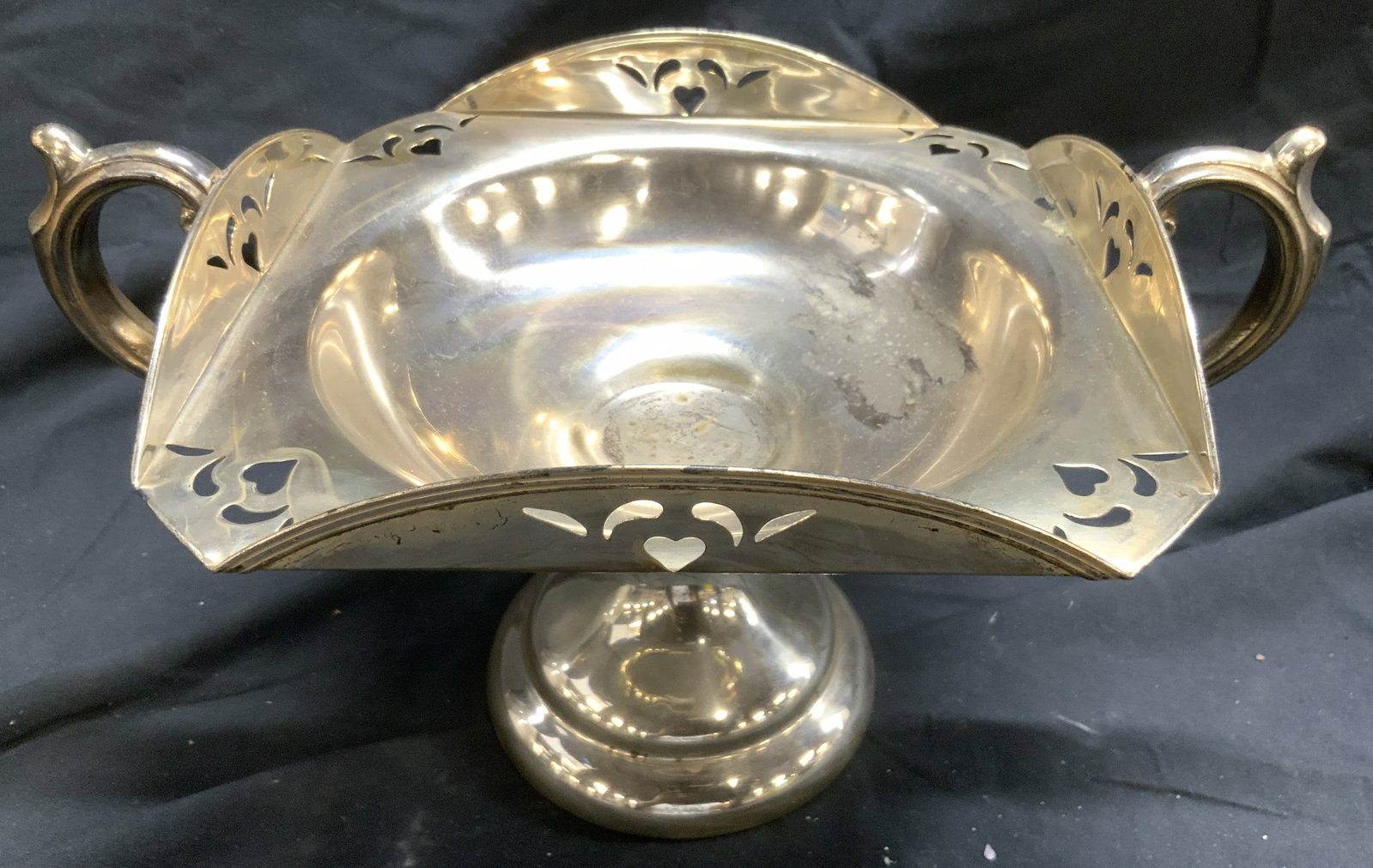 Silver Pl Pedestaled Vessel W Handles Raised Edges: Piece is silver plate. Vessel is pedestaled. Piece has c curl form handles. Vessel has raised edges and pierced detail. Piece is vintage. Vessel measures approx 7.5 inches tall 12.5 inches wide 8 inch