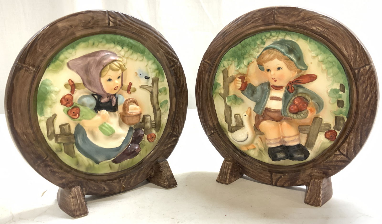 HUMMEL Lot 2 Vntg 3D Porcelain Plaques: Each piece appears to be HUMMEL (no apparent tag or markings). (C9047) Lot includes 2 porcelain plaques. Each have beveled 3 dimensional detail. One depicts a boy with a basket of apples and a duck, a
