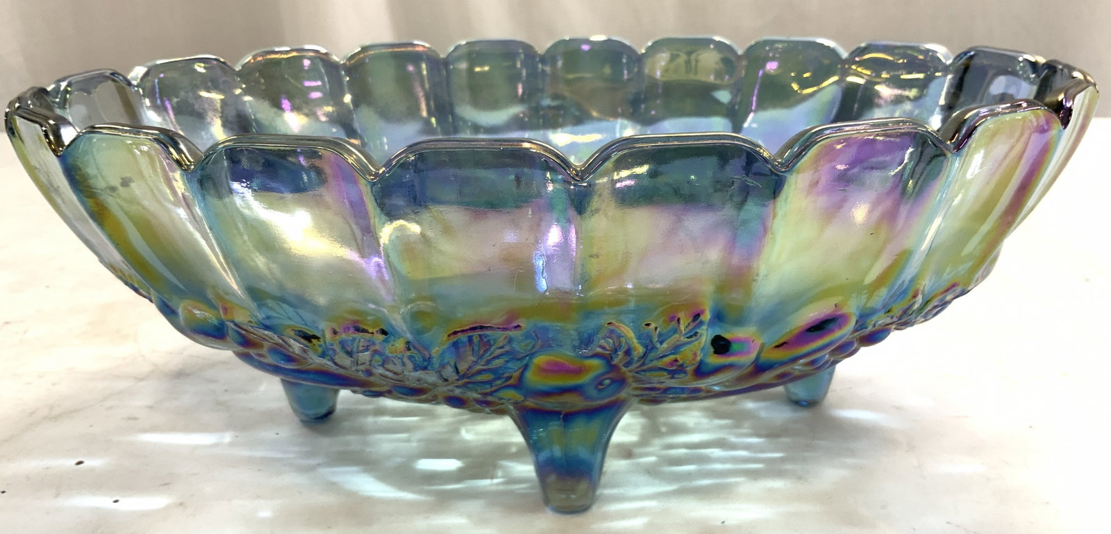 INDIANA Carnival Glass Iridescent Gls Footed Bowl: Bowl appears to be INDIANA GLASS COMPANY. Bowl has toothed rim. Piece has oval form. Bowl is footed. Piece has 4 feet. Bowl has beveled fruit and leaf detail to exterior. Piece has blue toned iridesce