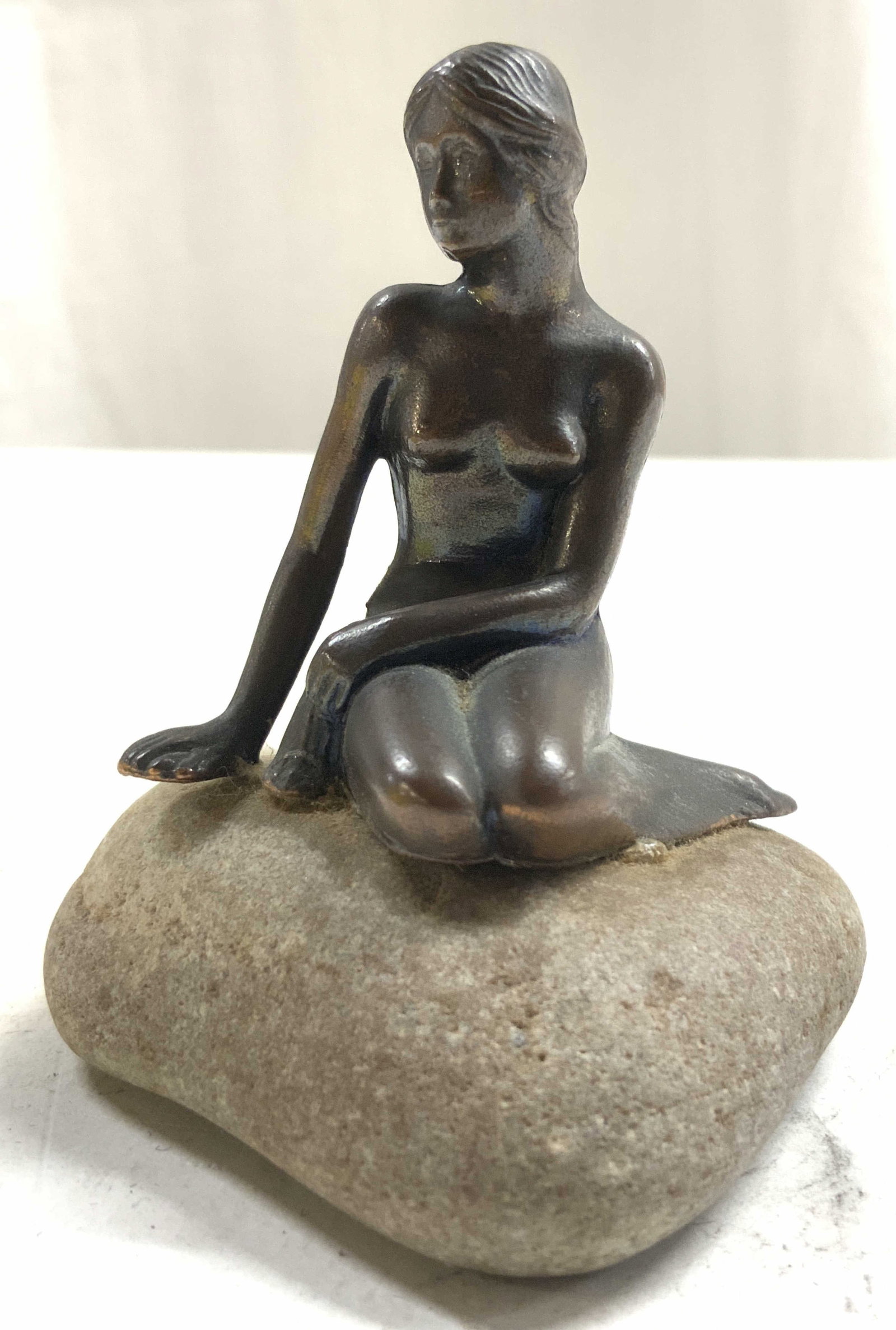 Copper Female Nude Figure On Rock: After the Little Mermaid by Edvard Eriksen. Piece is in the form of a female nude. Female figure is copper. Depicts figure kneeling. Base of piece is slate toned appears to be stone / cement. Piece me