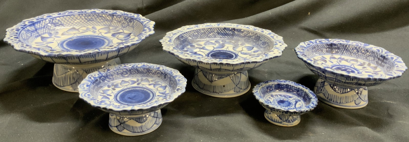 Set 5 Asian Chinoiserie Pedestaled Porc Dishes: Lot includes 5 dishes. Each are white toned and porcelain with blue toned floral, leaf & patterned detail. Asian Pedestaled chinoiserie dishes. Each have uniquely formed rims. Largest dish measures ap