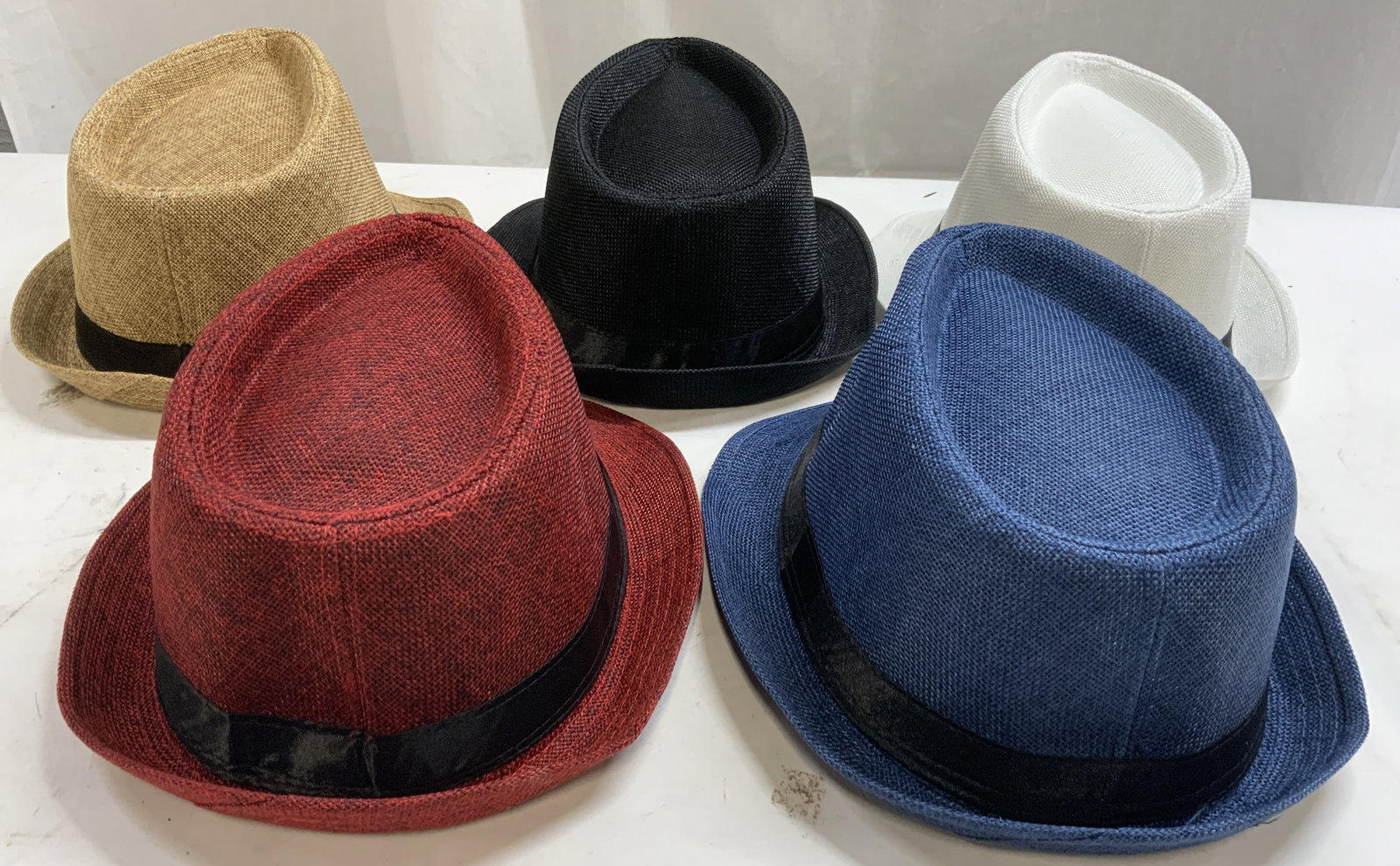 Lot 5 Woven Poly Cotton Fedoras: Lot includes 5 Fedoras. Each hat is brimmed with black toned band. Tags each read 60. Lot includes 1 red, 1 blue, 1 beige, 1 black, & 1 white toned hat. Each are polyester & cotton. Hats each measure