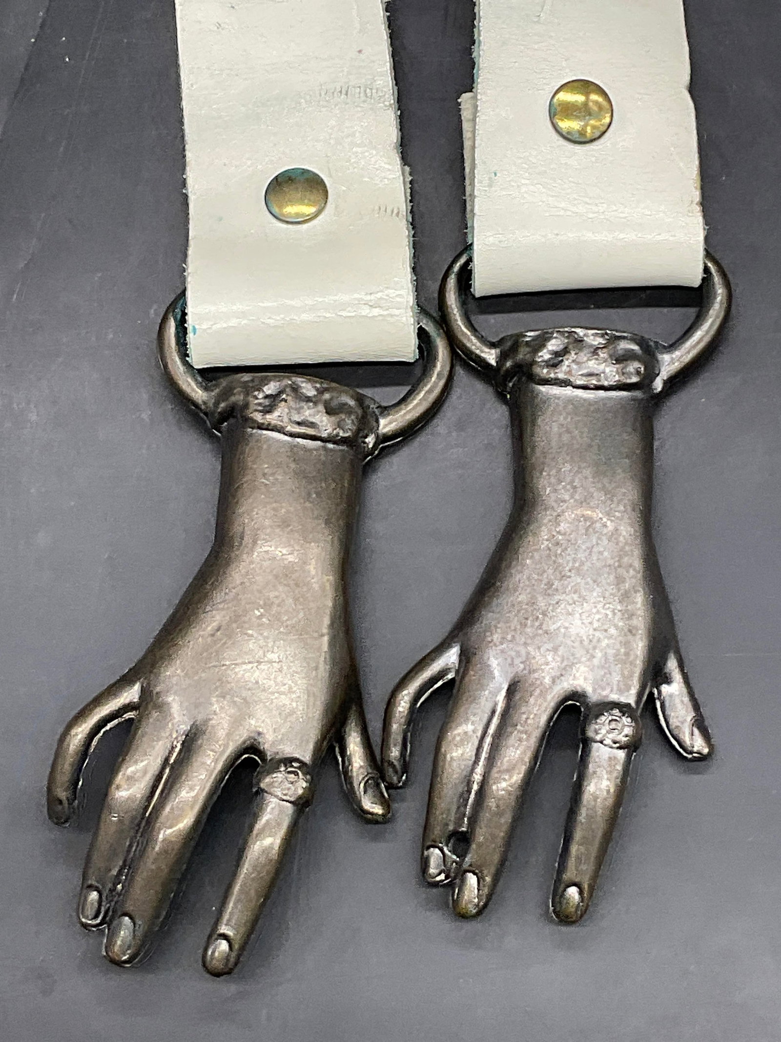 Vintage Metal Hand Motif Buckle White Belt: Vintage Metal Hand Motif Buckle White Belt. Total length approx. 36 inches in length. Belt is possibly crafted from leather or leather style material. Patina to the hands. Discoloration, surface wear,