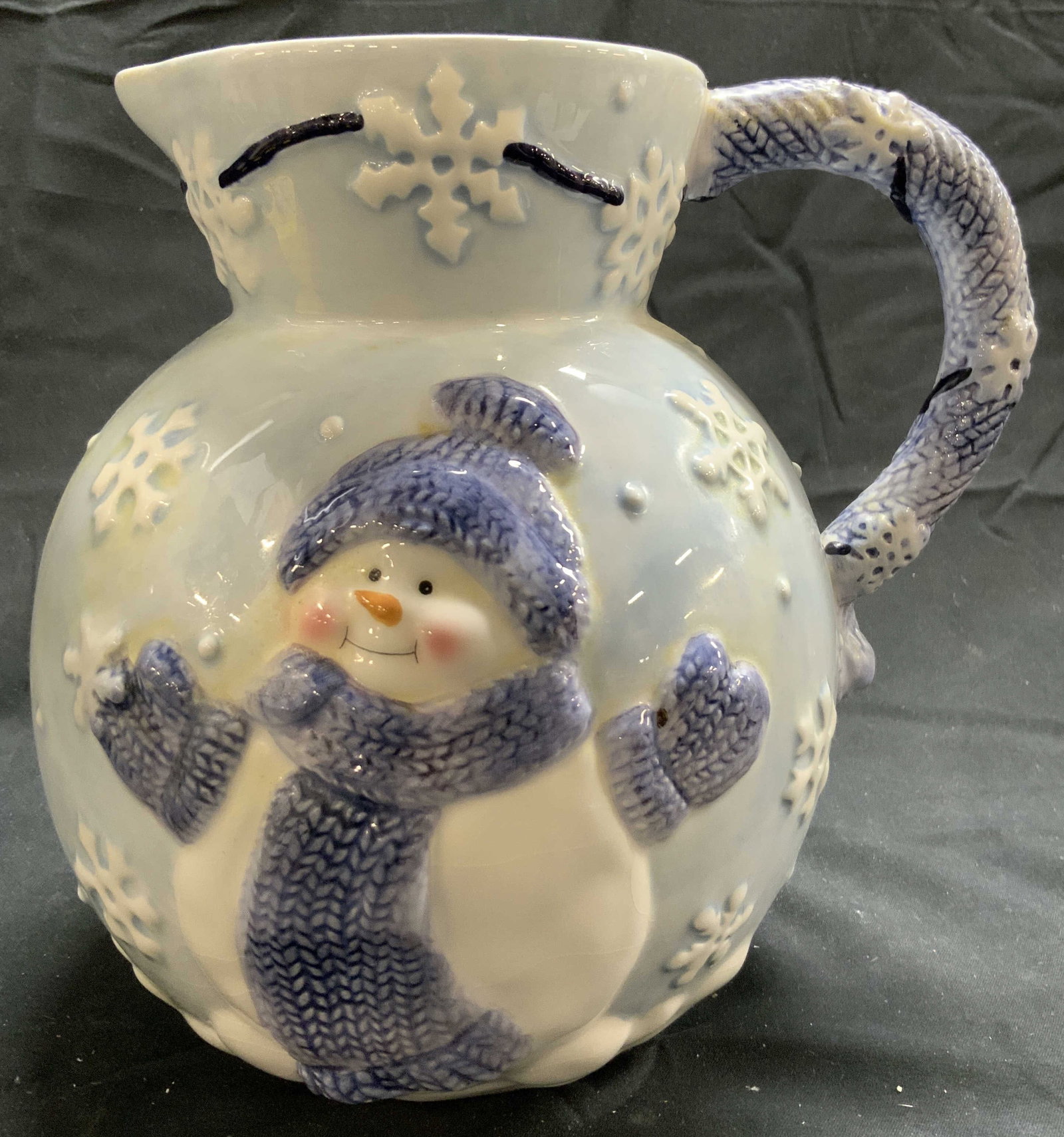 BELLA CASA Porcelain Snowman Pitcher: Underside is marked BELLA CASA BY GANZ. Pitcher is porcelain. Piece has snowflake and snowman detail. Piece has light blue and white tones. Pitcher has textured handle. Piece measures approximately 7.