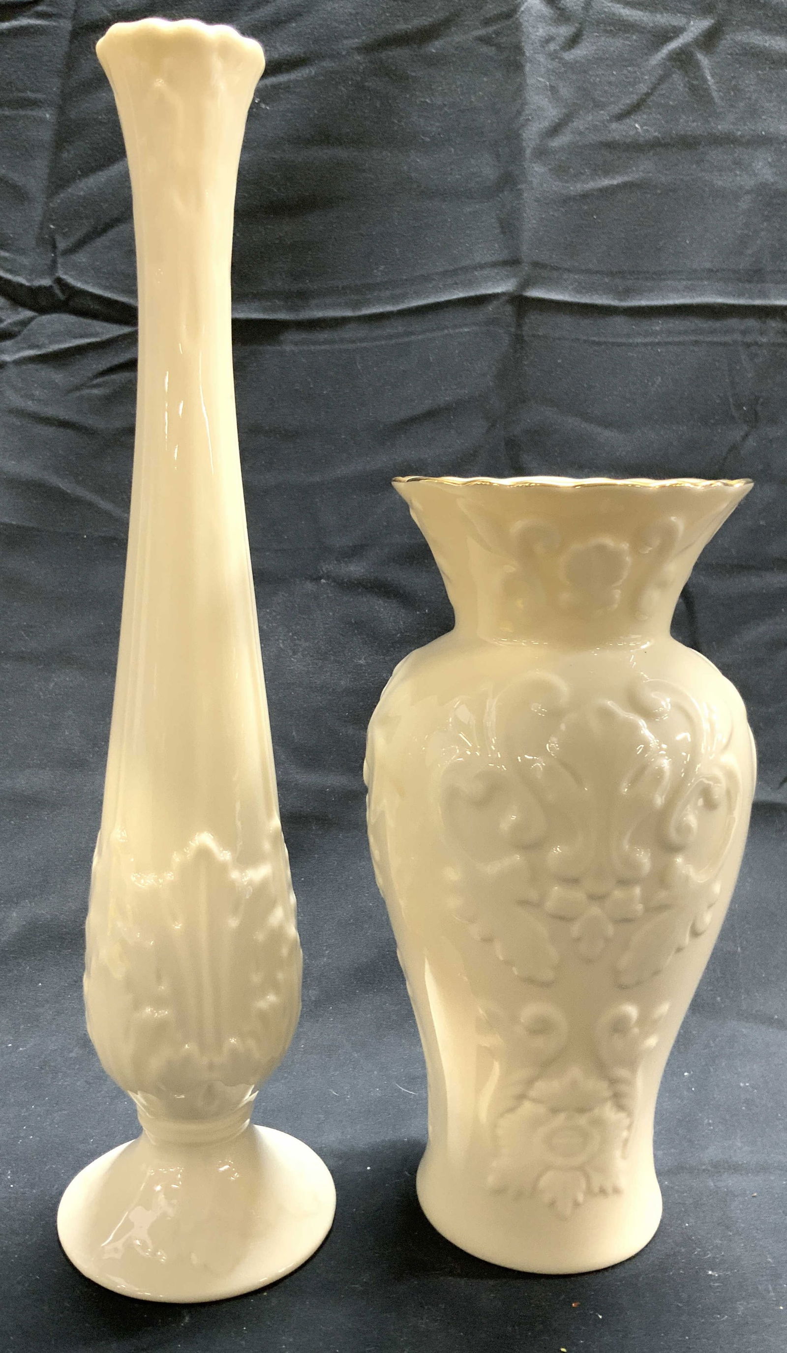 LENOX Lot 2 Porcelain Vases Vessels: Undersides of each vase are marked LENOX. Lot includes 2 vases, each are cream toned and porcelain. One vase is footed. The other vase has gilt rim. Vase with gilt rim has beveled scroll & leaf detail