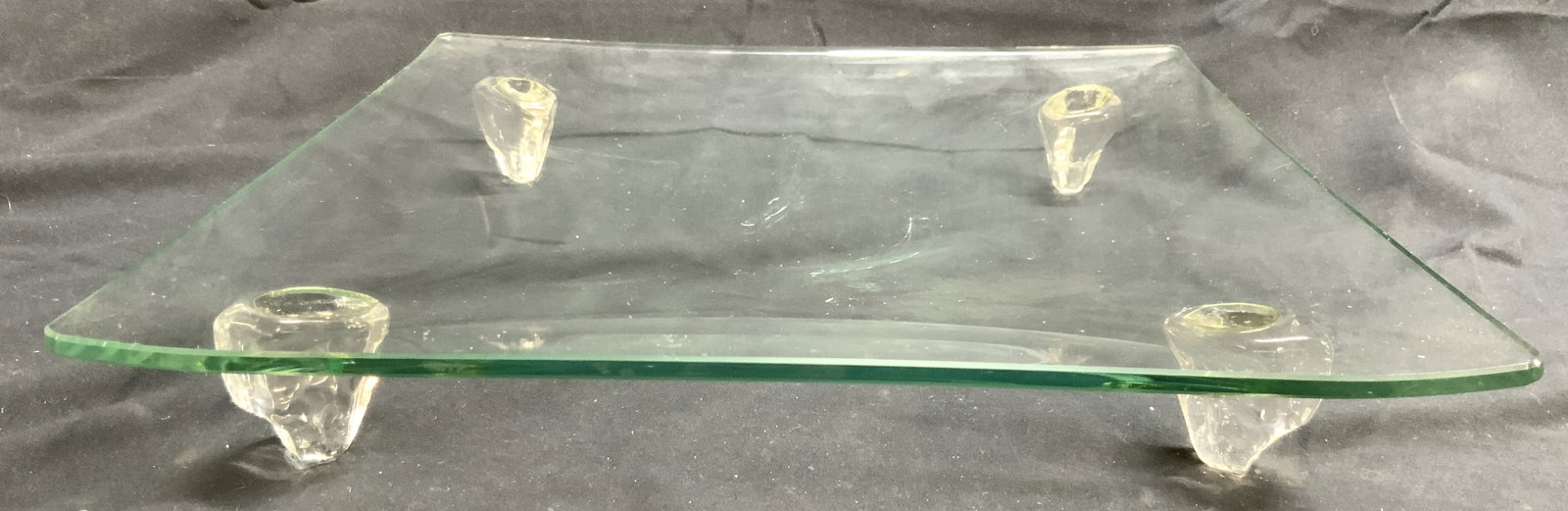 Footed Glass Tabletop Centerpiece Tray: Centerpiece tray is footed with 4 feet. Piece is glass. Tray has square form. Piece is slightly concave. Tray measures approximately 12 inches square 2 inches tall. Tray, glass tray, footed tray, tabl