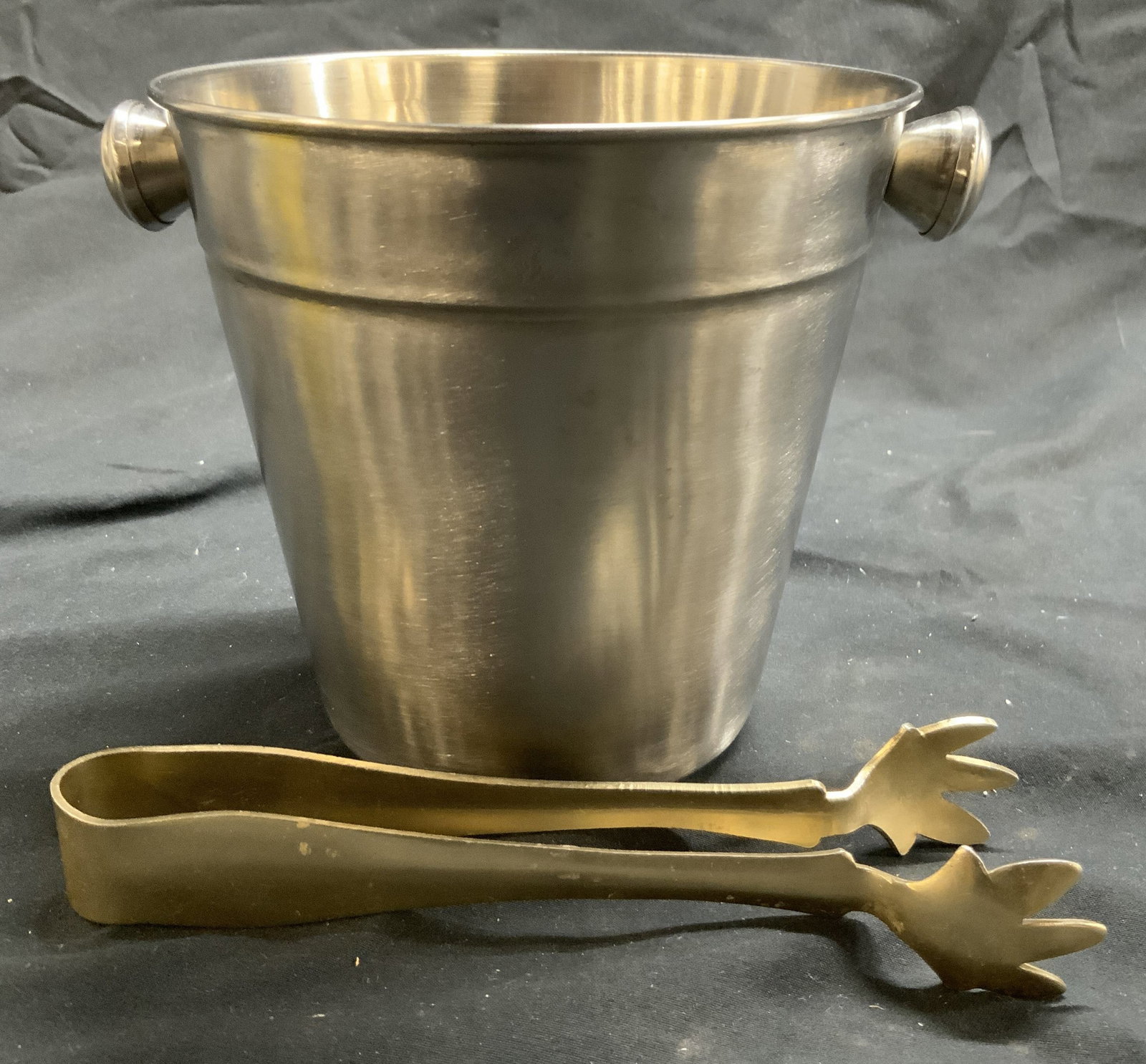 Brushed Metal Ice Bucket W Tongs: Lot includes 1 ice bucket & 1 pair of tongs. Each piece is brushed metal. Tongs have claw ends. Ice bucket is silver toned with knob form handles at sides. Piece measures approximately 6.5 inches wide