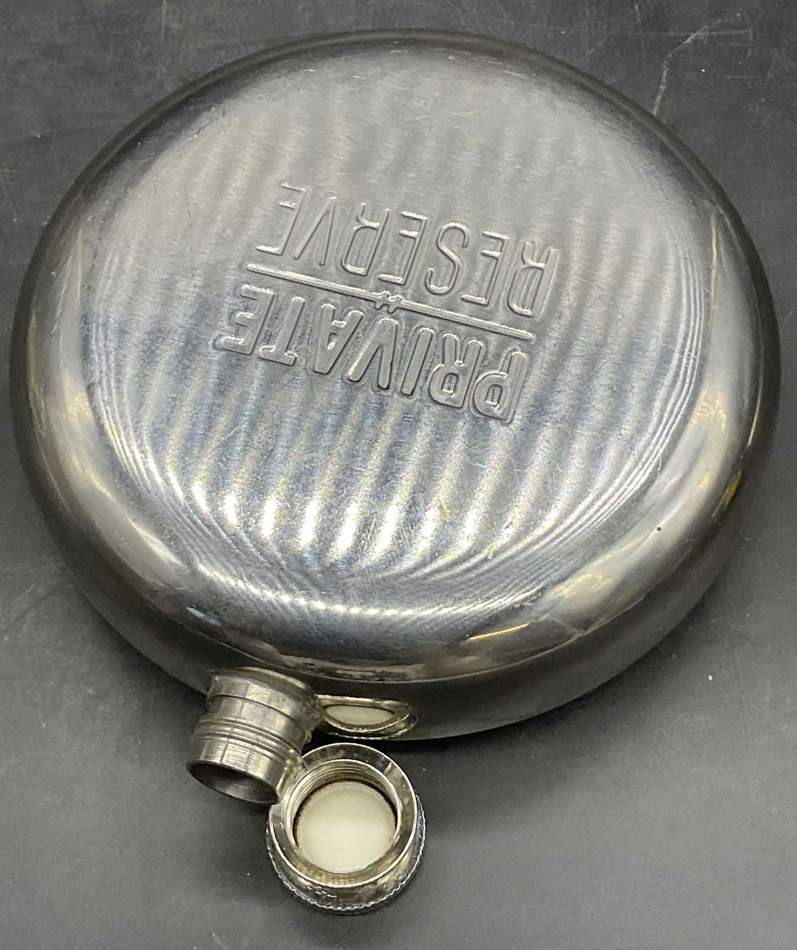 PRIVATE RESERVE Stainless Steel 10oz Flask: PRIVATE RESERVE Stainless Steel 10oz Flask. Twist off lid. Obverse and reverse read PRIVATE RESERVE. Underside reads Stainless Steel 10oz. Measures approx. 5L x 4.25W in. Surface wear consistent with